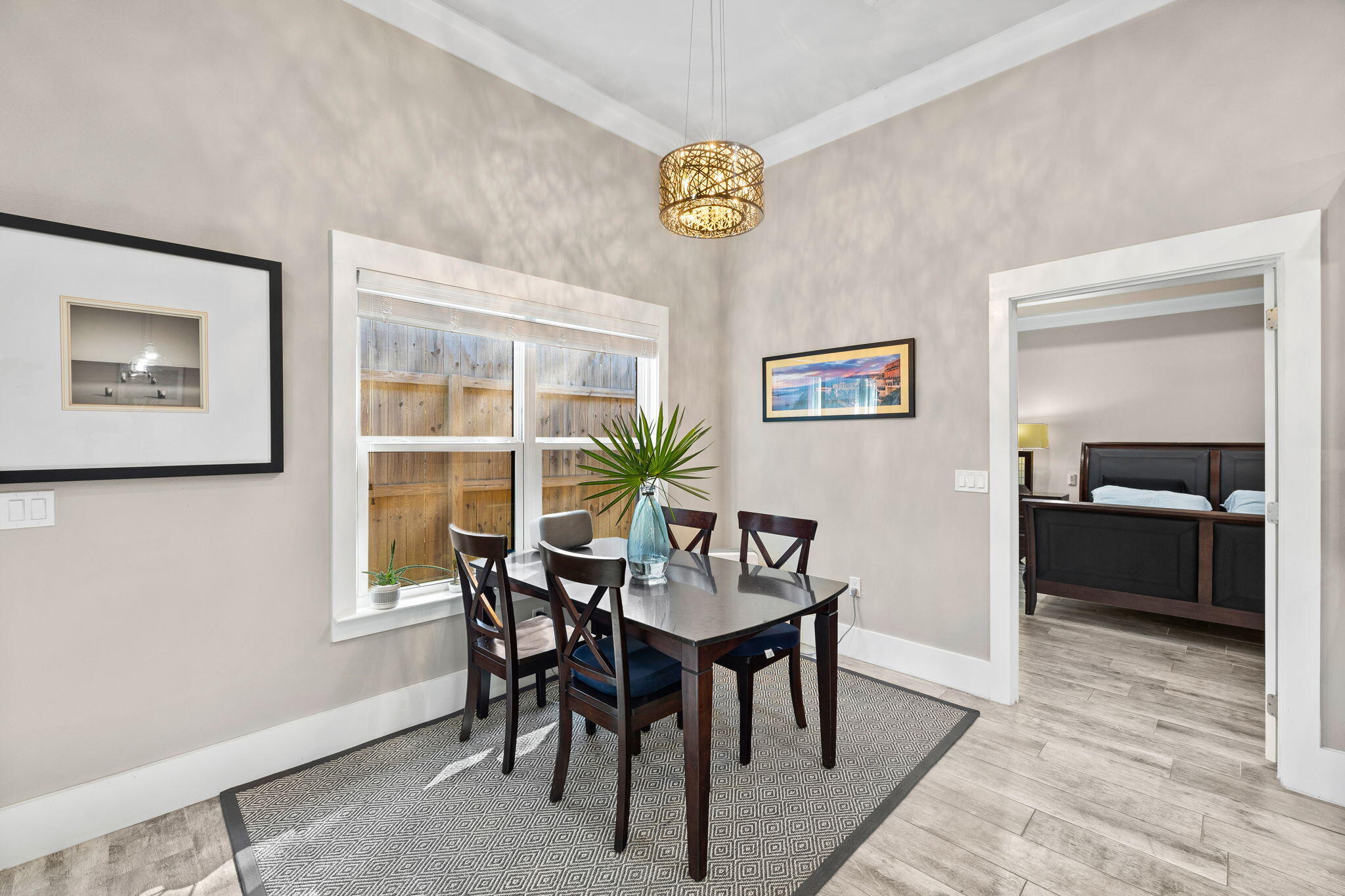 Dining room with a dark wood table, patterned rug, and adjoining bedroom visible through an open doorway.