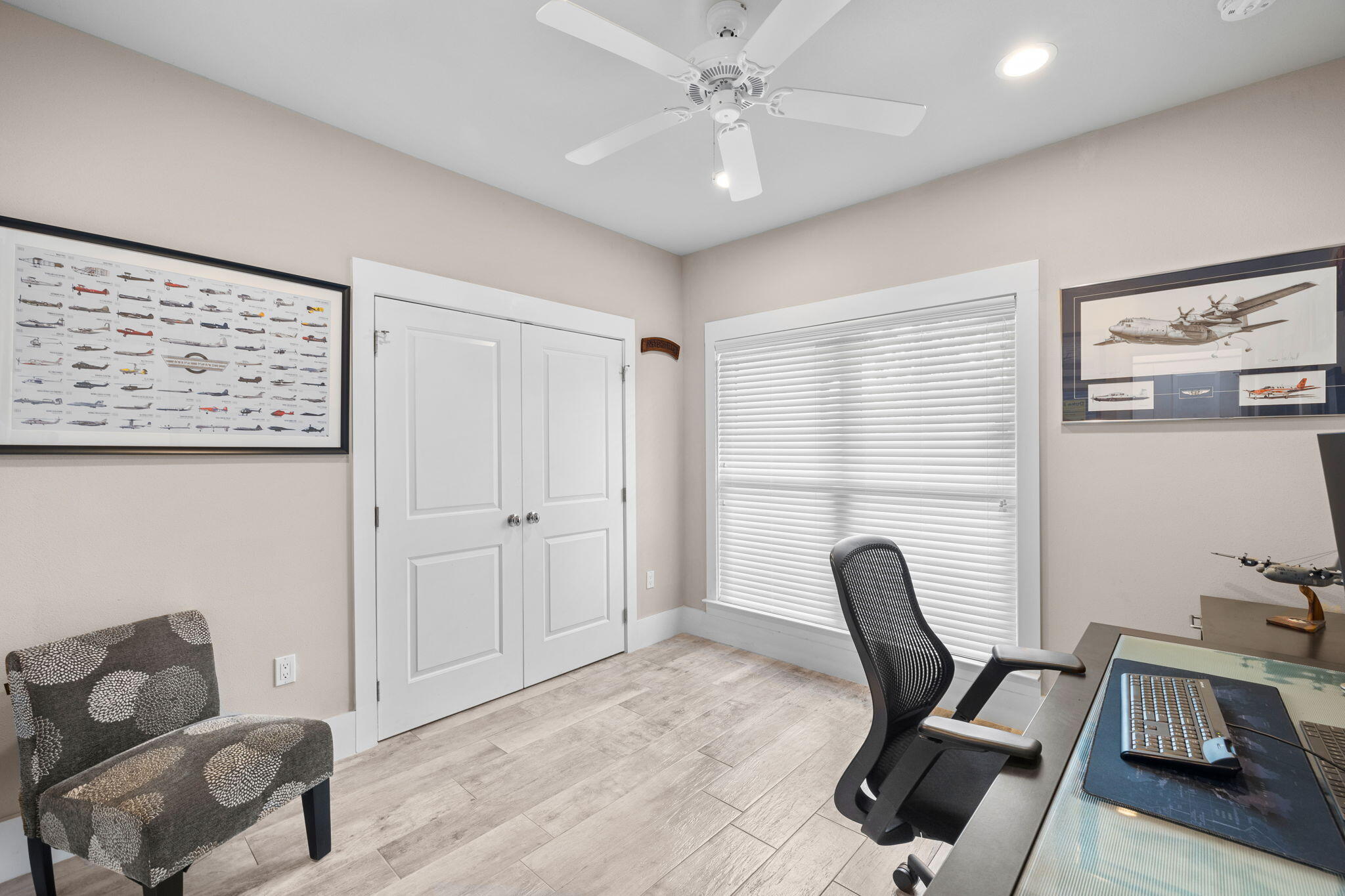 Furnished home office with framed airplane illustrations, a desk, and a patterned accent chair.