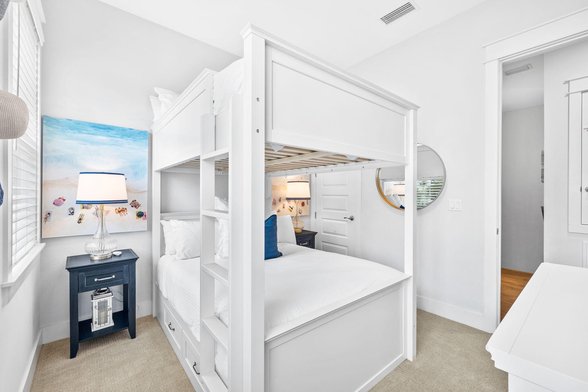 Bright bedroom with a white built-in bunk bed, beach-themed artwork, and navy bedside table.
