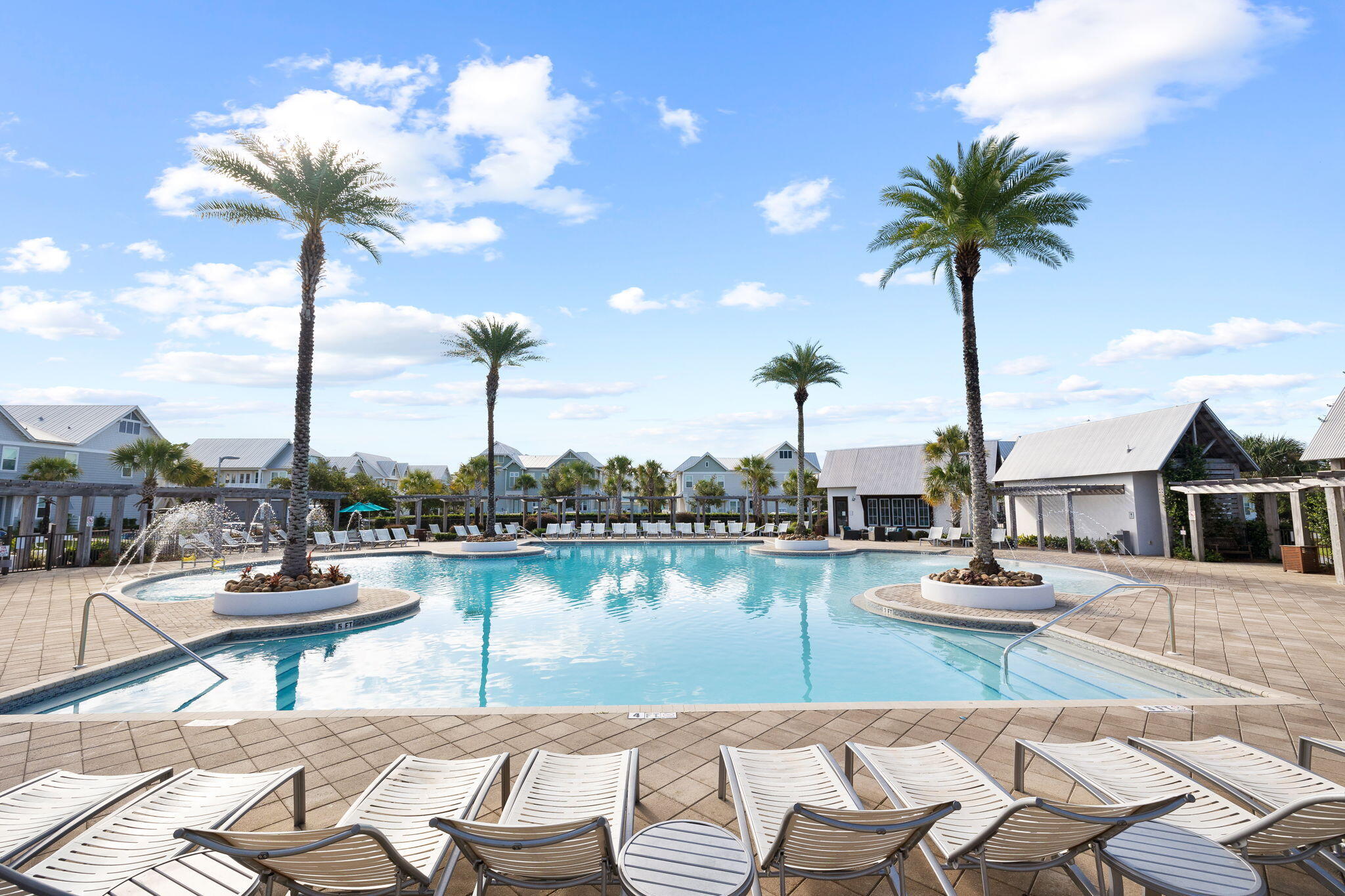 Community pool with palm-tree islands, fountains, and rows of white loungers.