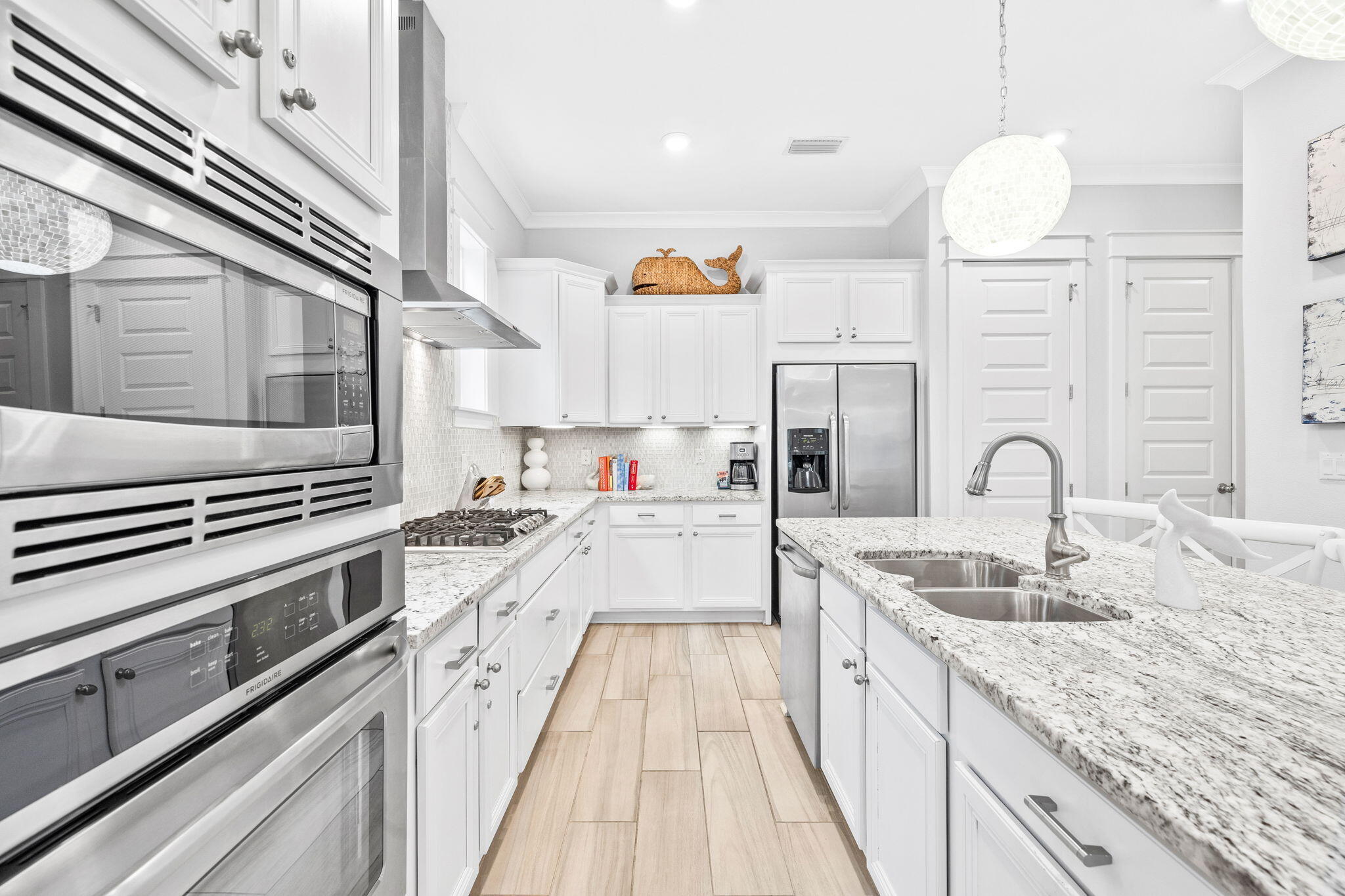 Bright white kitchen with stainless double ovens and a granite island with a double sink.