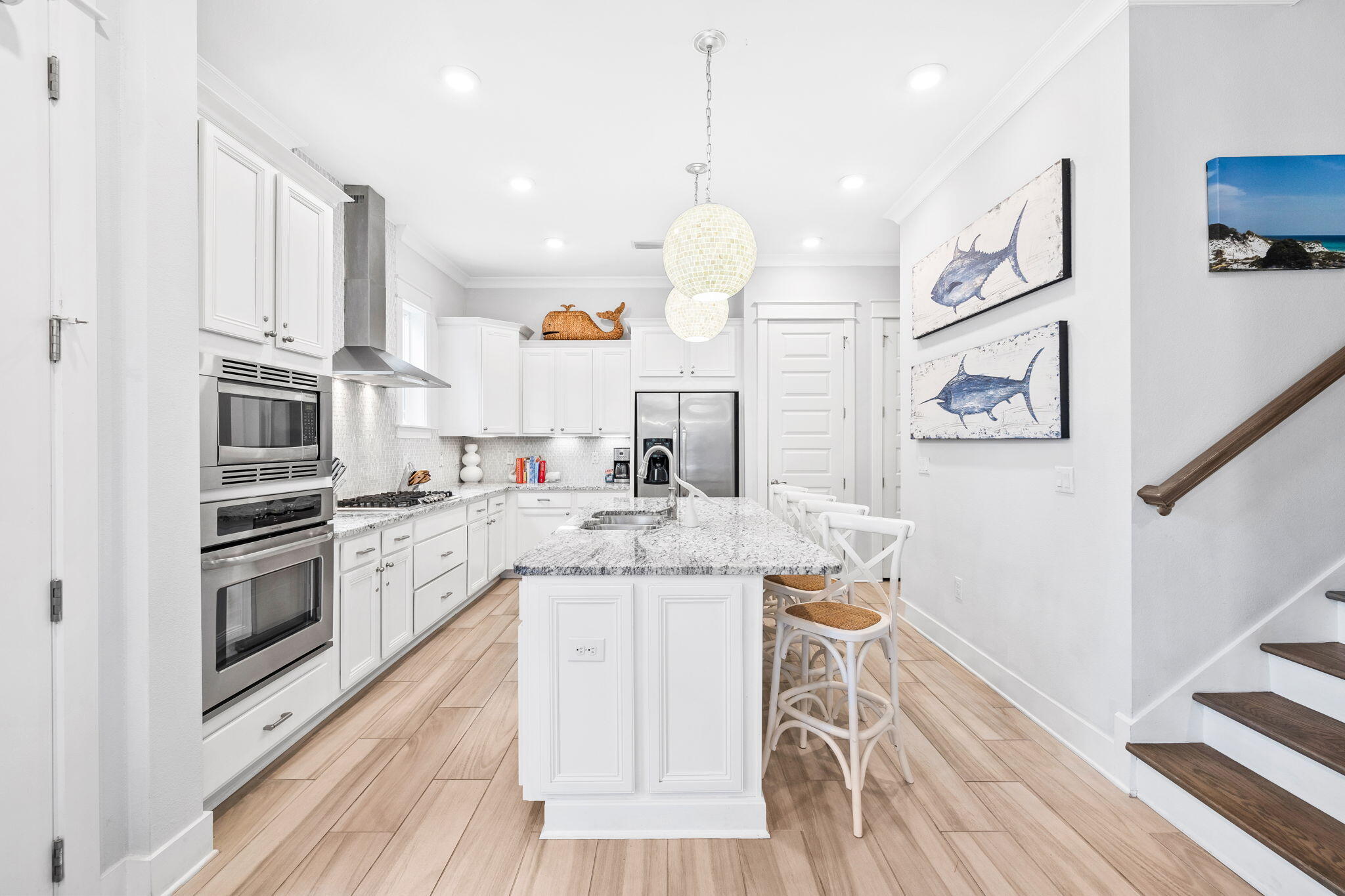 Bright white kitchen with a granite island, stainless steel appliances, and stairs along the right side.