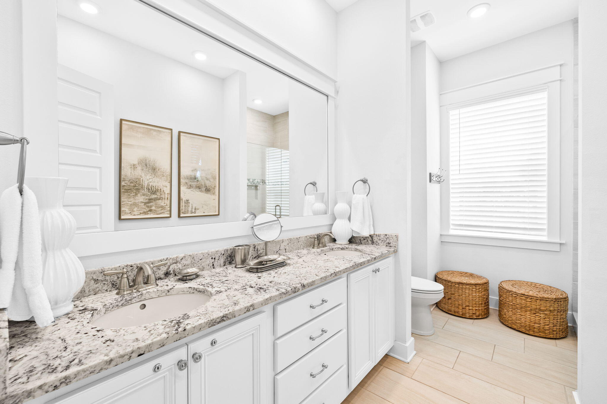 Bathroom with a long granite-topped vanity, large mirror, and woven baskets beside the toilet.