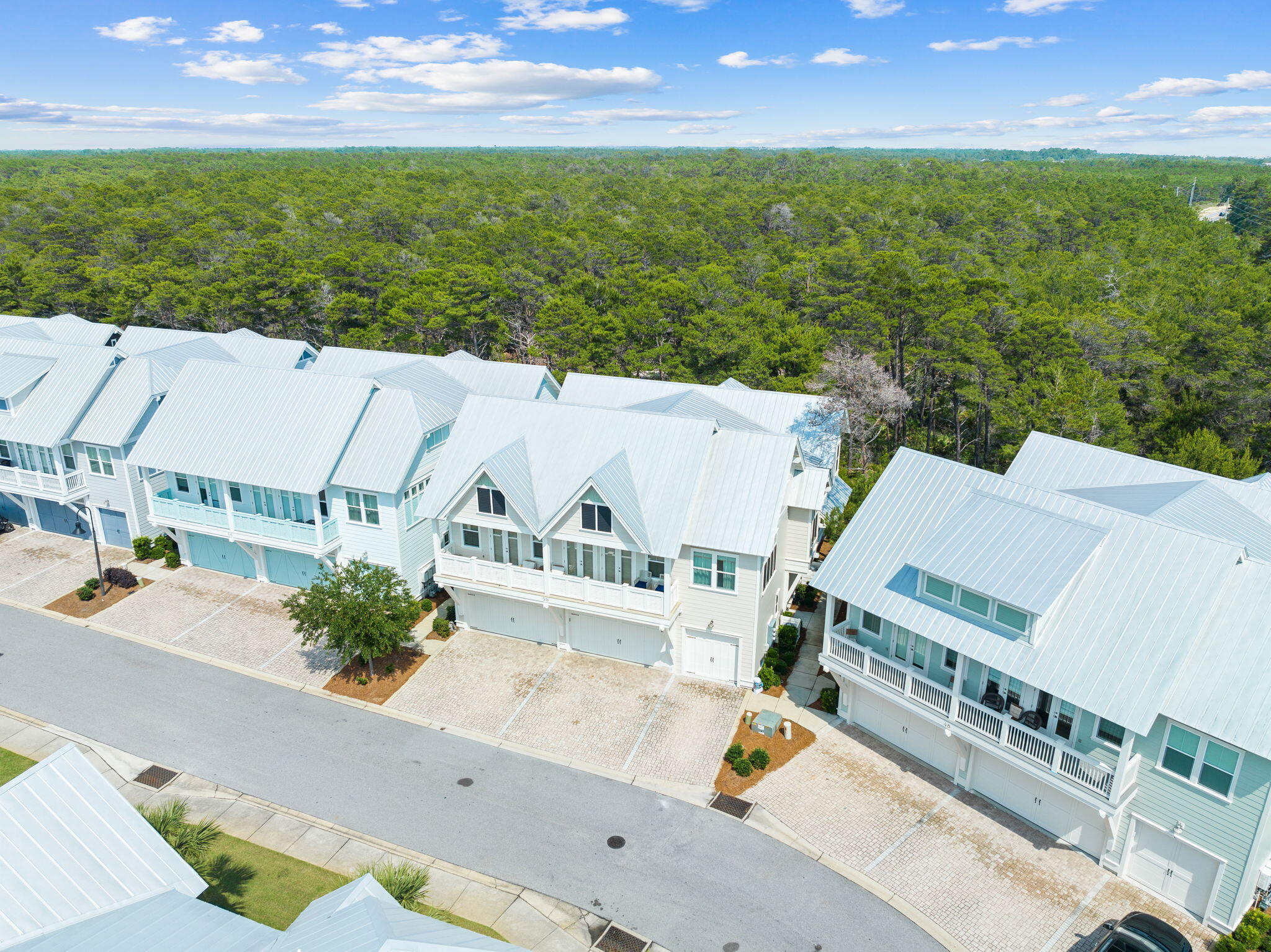 Aerial view of white-roofed townhomes beside a dense green forest.