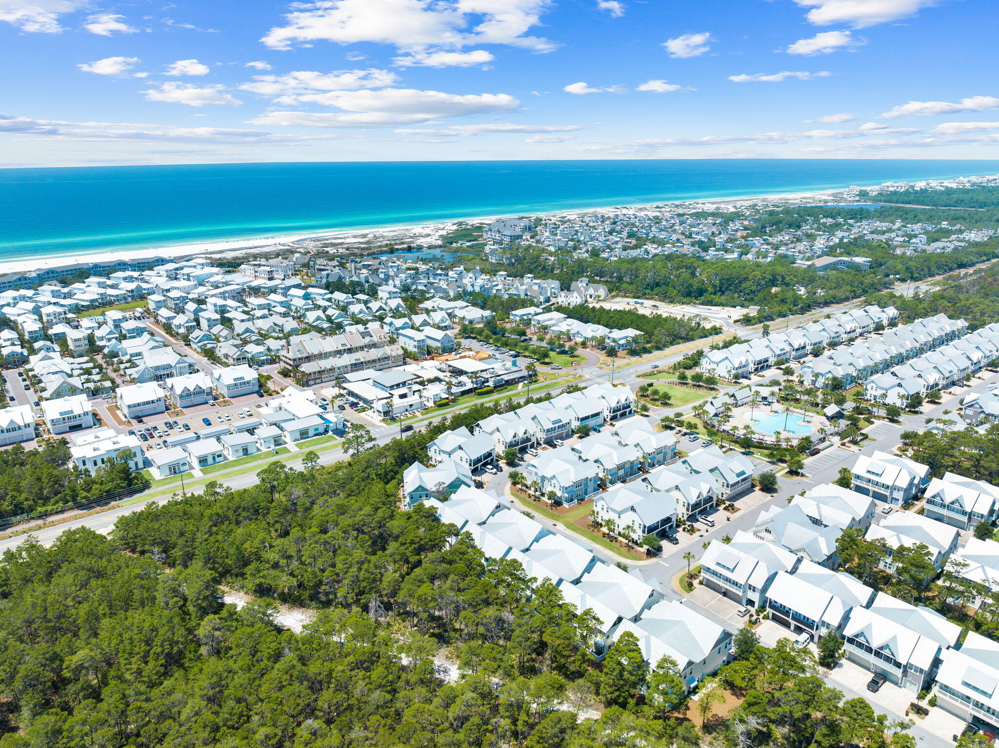 Aerial coastal neighborhood with white-roofed homes, a community pool, and turquoise water beyond the beach.