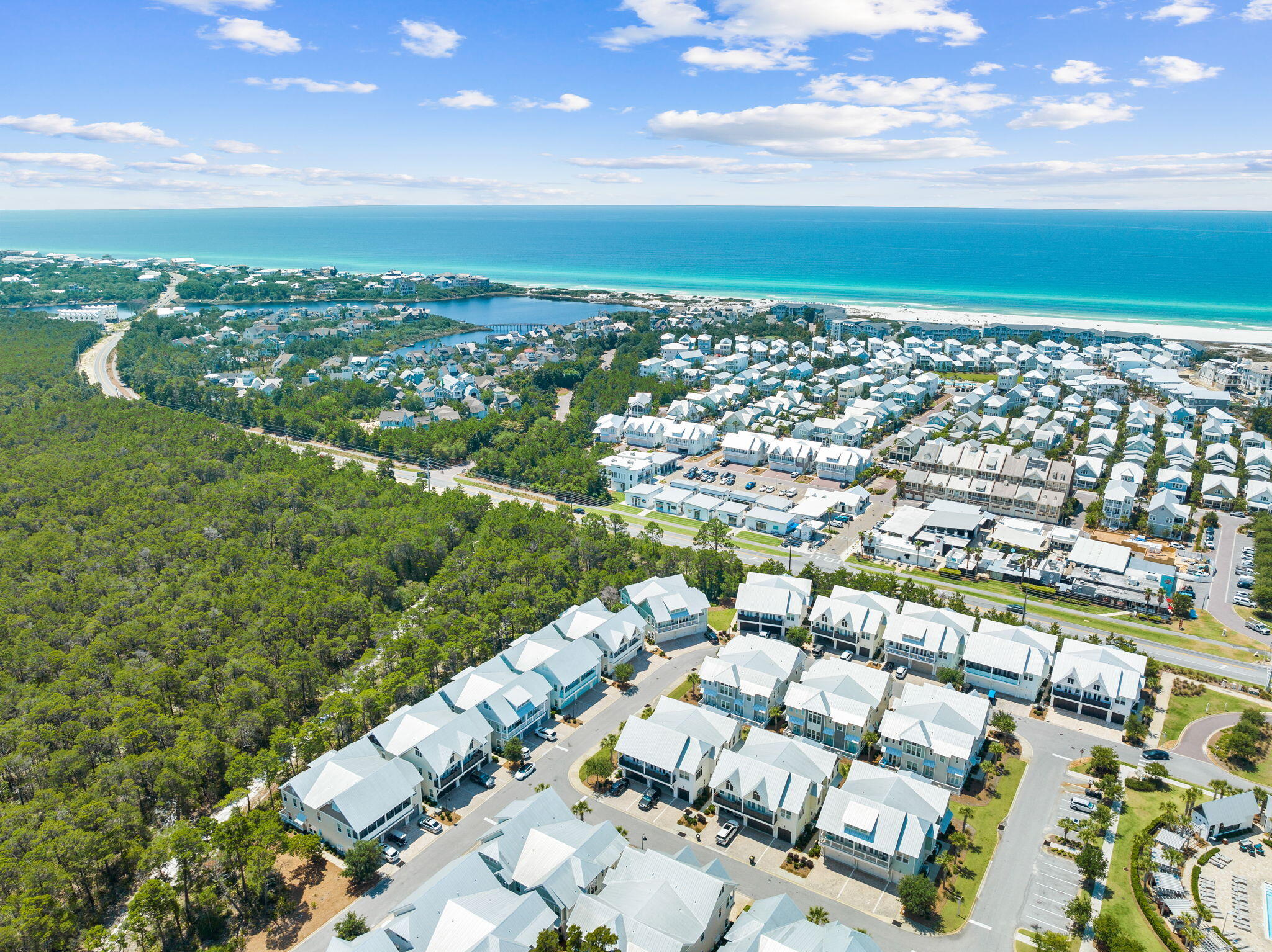 Aerial view of coastal homes, wooded land, a lagoon, and turquoise ocean along a sandy beach.