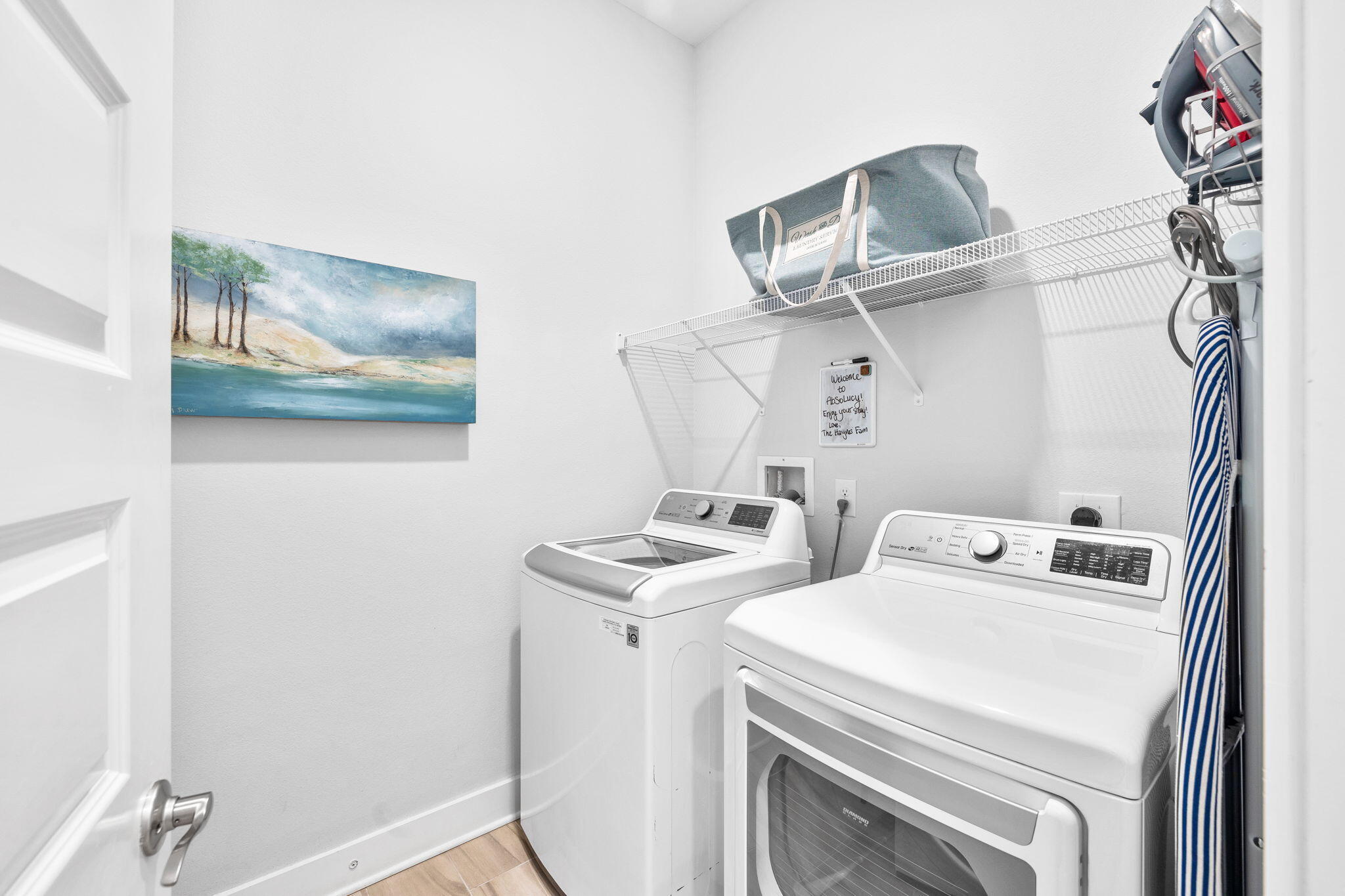 Laundry room with a white washer and dryer, wire shelving, and a striped ironing board.