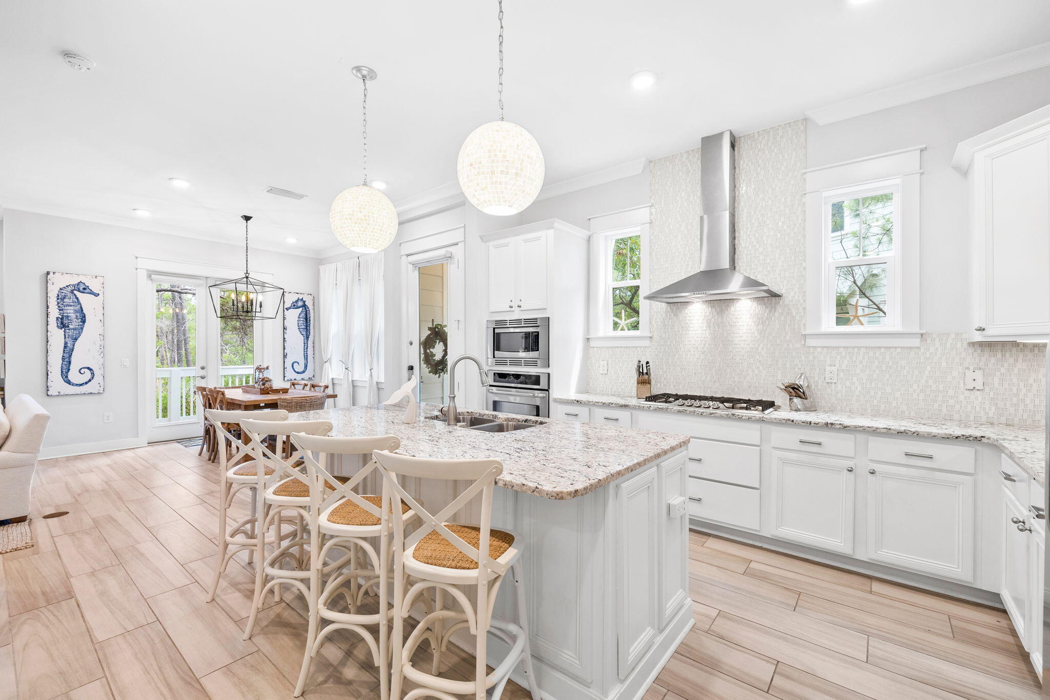 Bright white kitchen with a granite island, white bar stools, stainless appliances, and adjoining dining area.