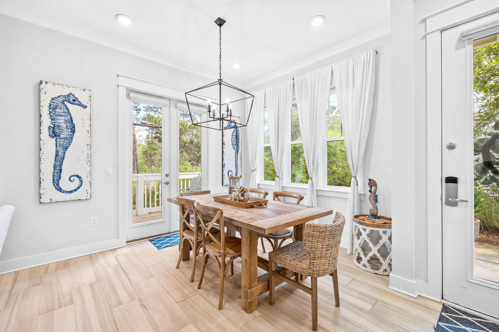 Dining room with a rustic wood table, woven chairs, seahorse artwork, and glass doors opening to a deck.
