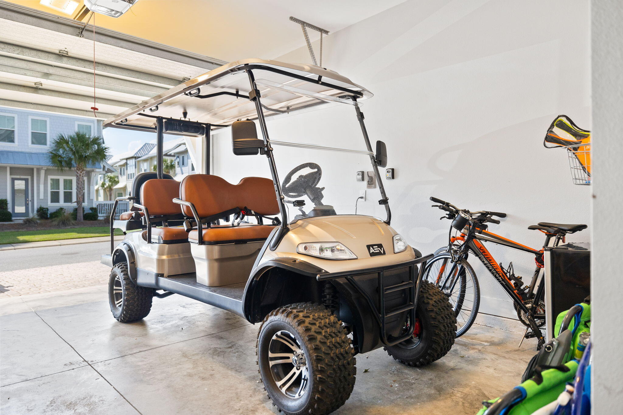 Golf cart and bicycles parked in a garage with the door open to the street.