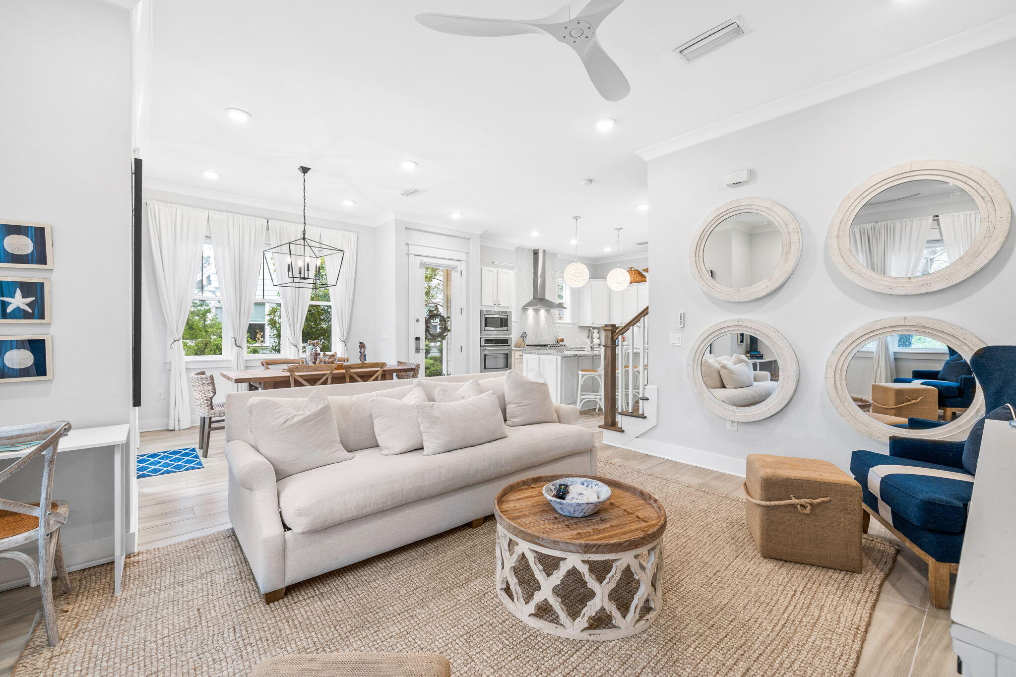 Open-plan living room with a white sofa, woven rug, and round mirrors above navy armchairs.