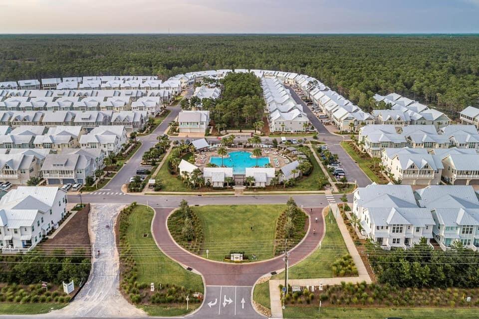 Coastal community with white-roofed homes surrounding a central pool, forest, and ocean horizon.