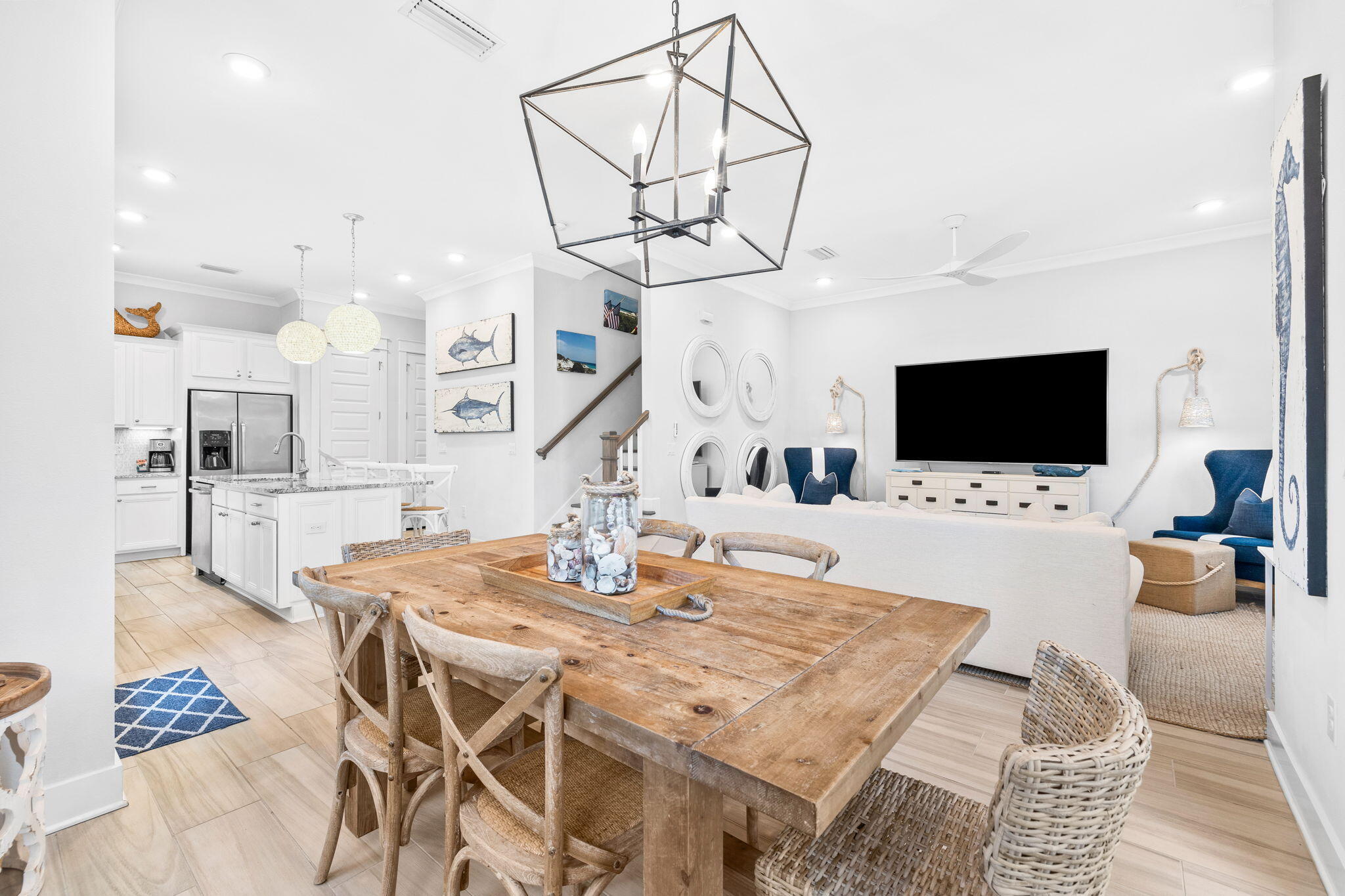 Open-plan dining, kitchen, and living area with a rustic wood table and blue accent chairs.