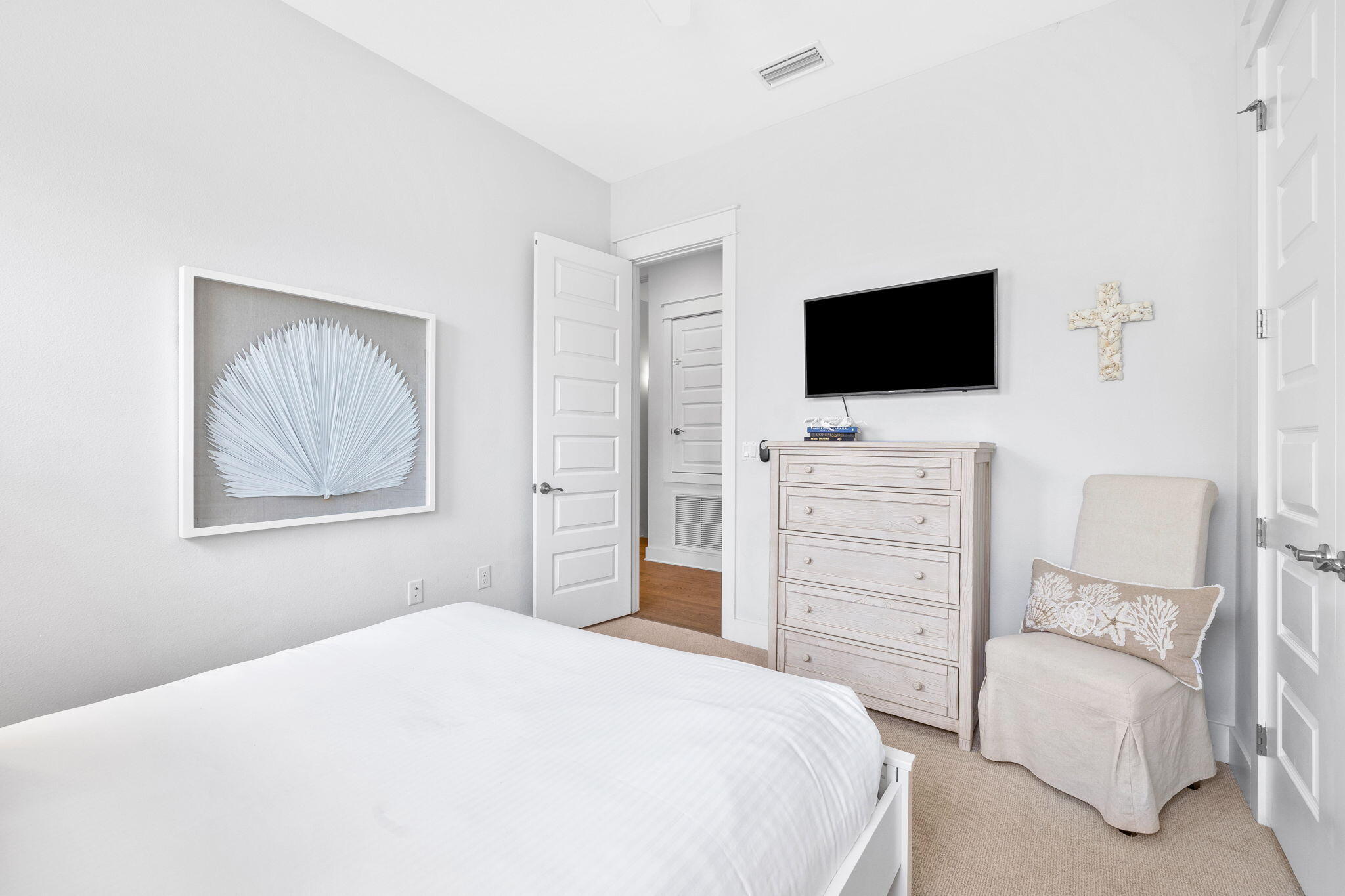 Bright bedroom with a white bed, pale wood dresser, and upholstered armchair.