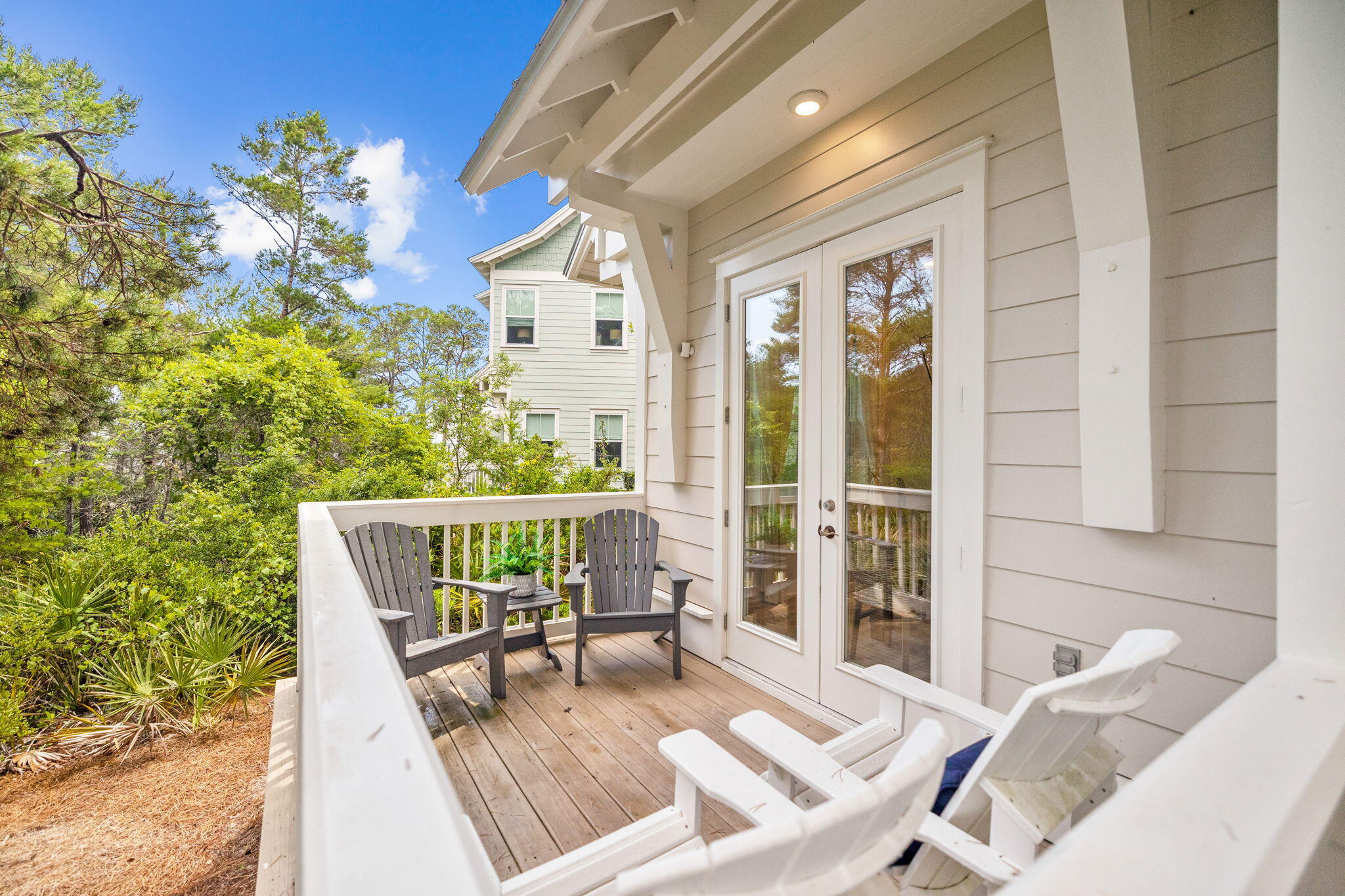 Raised wooden deck with Adirondack chairs, white railings, and French doors, surrounded by trees.
