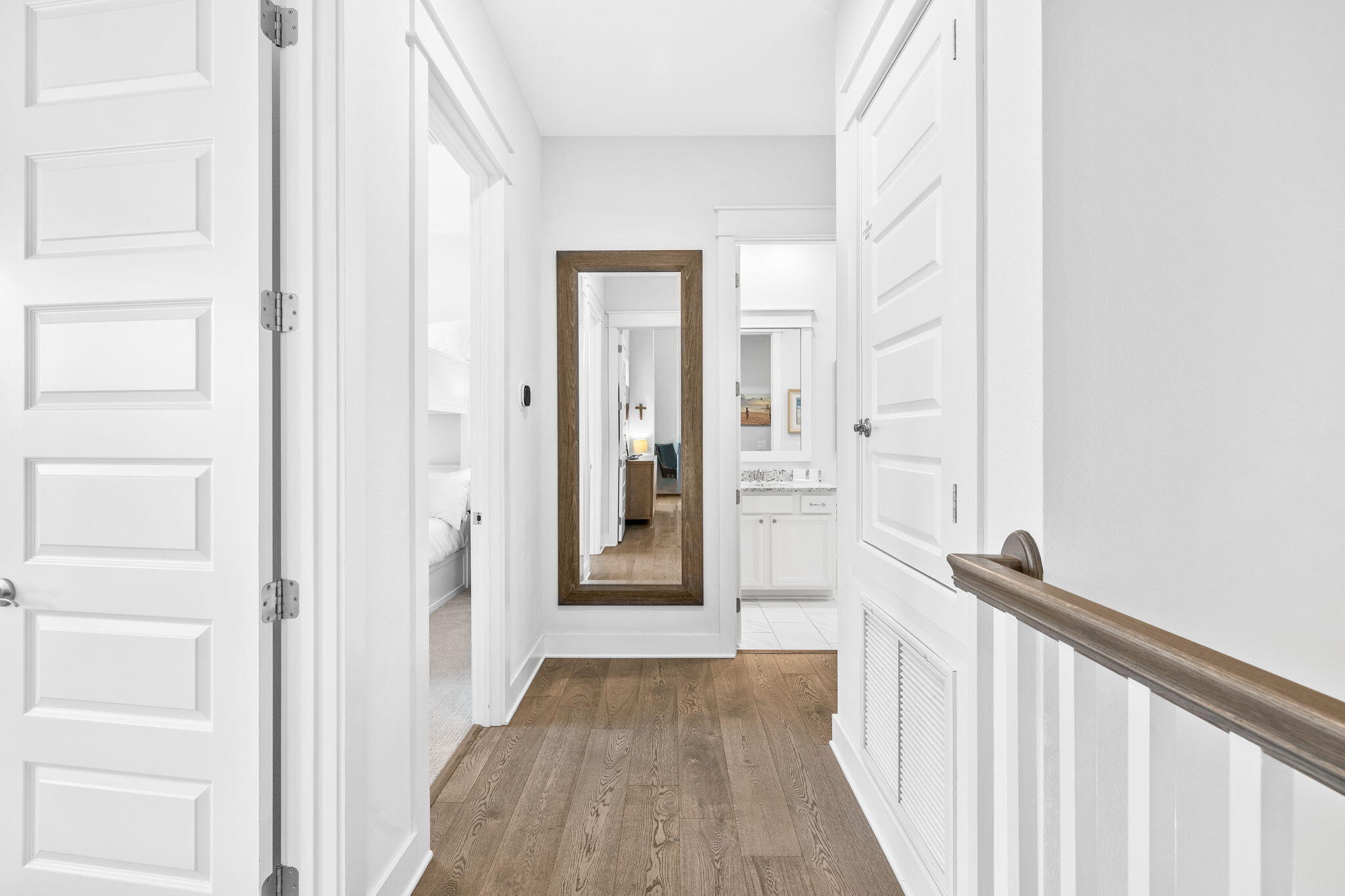 Hallway with wood floors, white paneled doors, and a large wood-framed mirror.