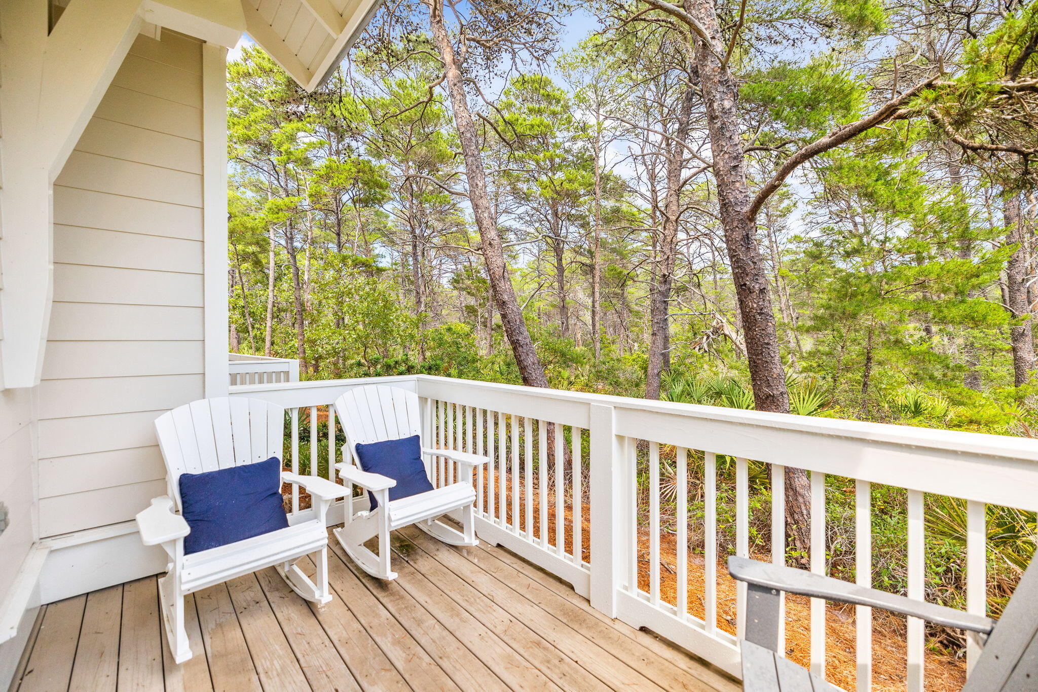 Wooden balcony with white rocking chairs and navy cushions overlooking a wooded area.