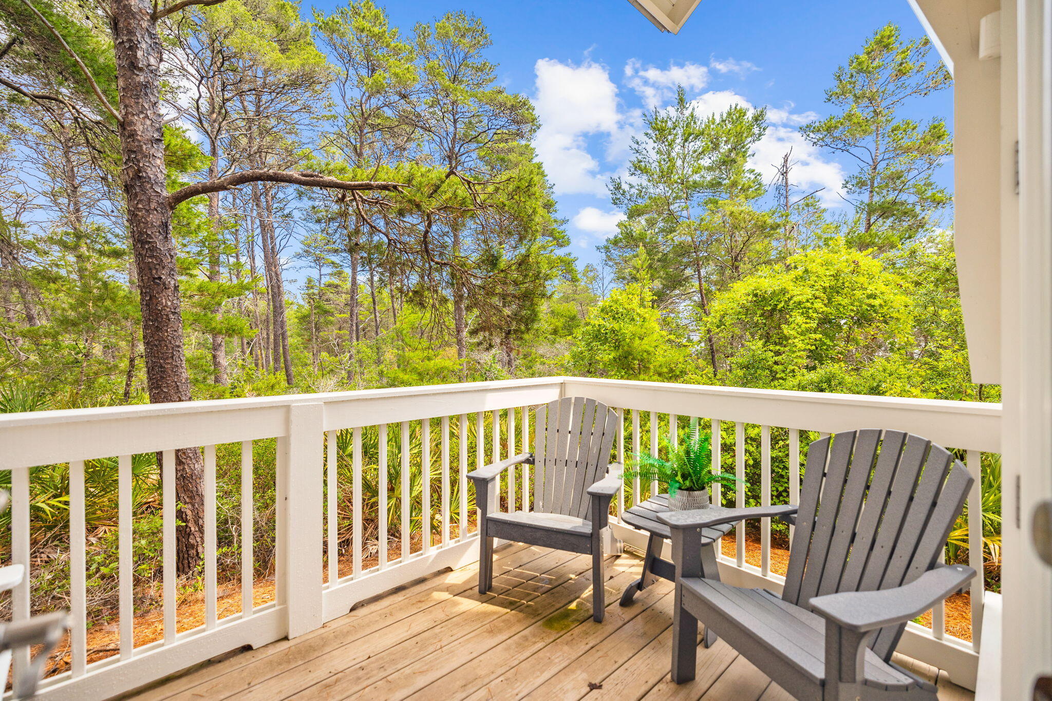 Wooden deck with two gray Adirondack chairs overlooking a leafy wooded area.