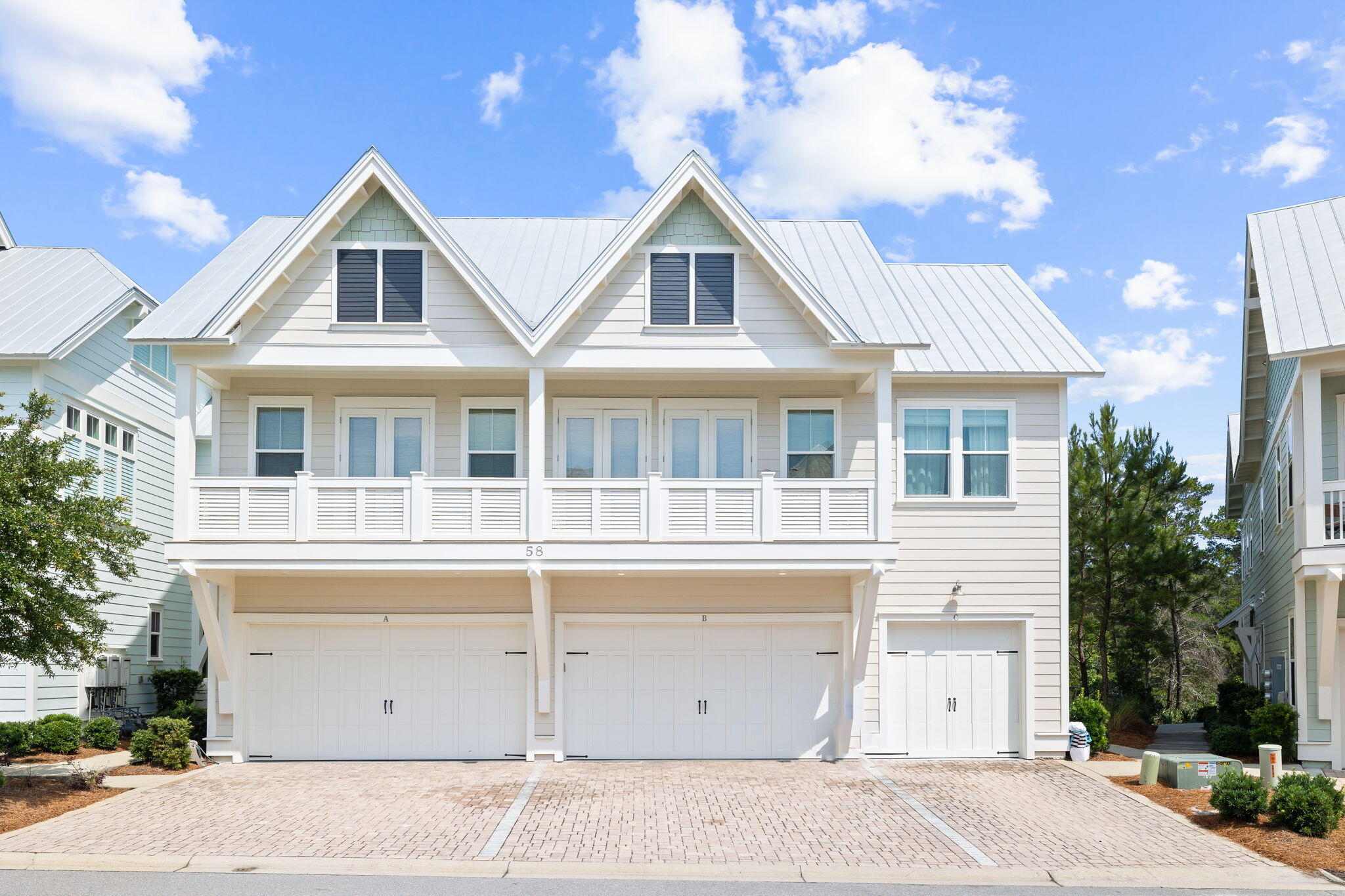 White multi-unit home with twin front gables, balcony railings, metal roof, and paved driveway.