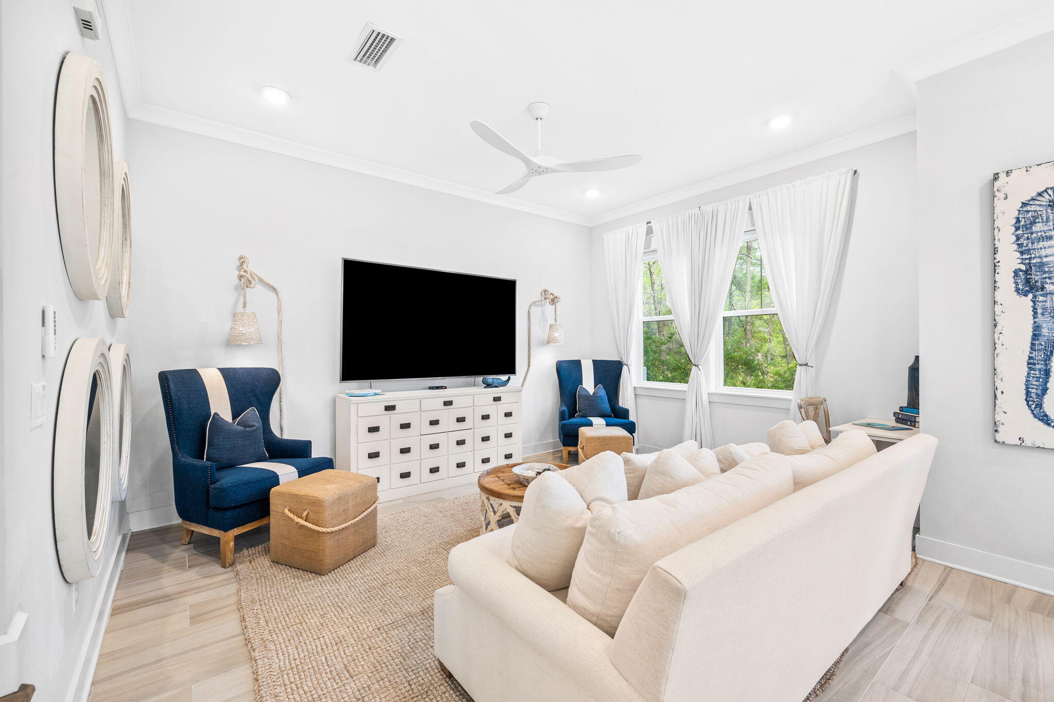 Living room with a white sectional, navy armchairs, and curtained windows overlooking greenery.