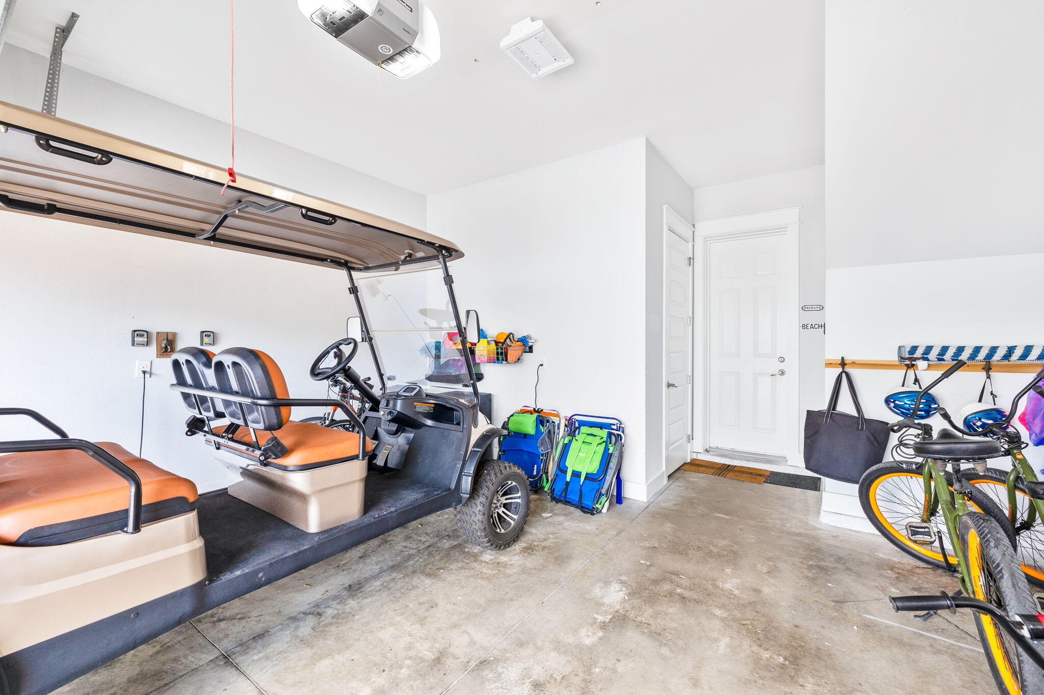 Garage with a golf cart, bicycles, and beach gear beside the entry door.