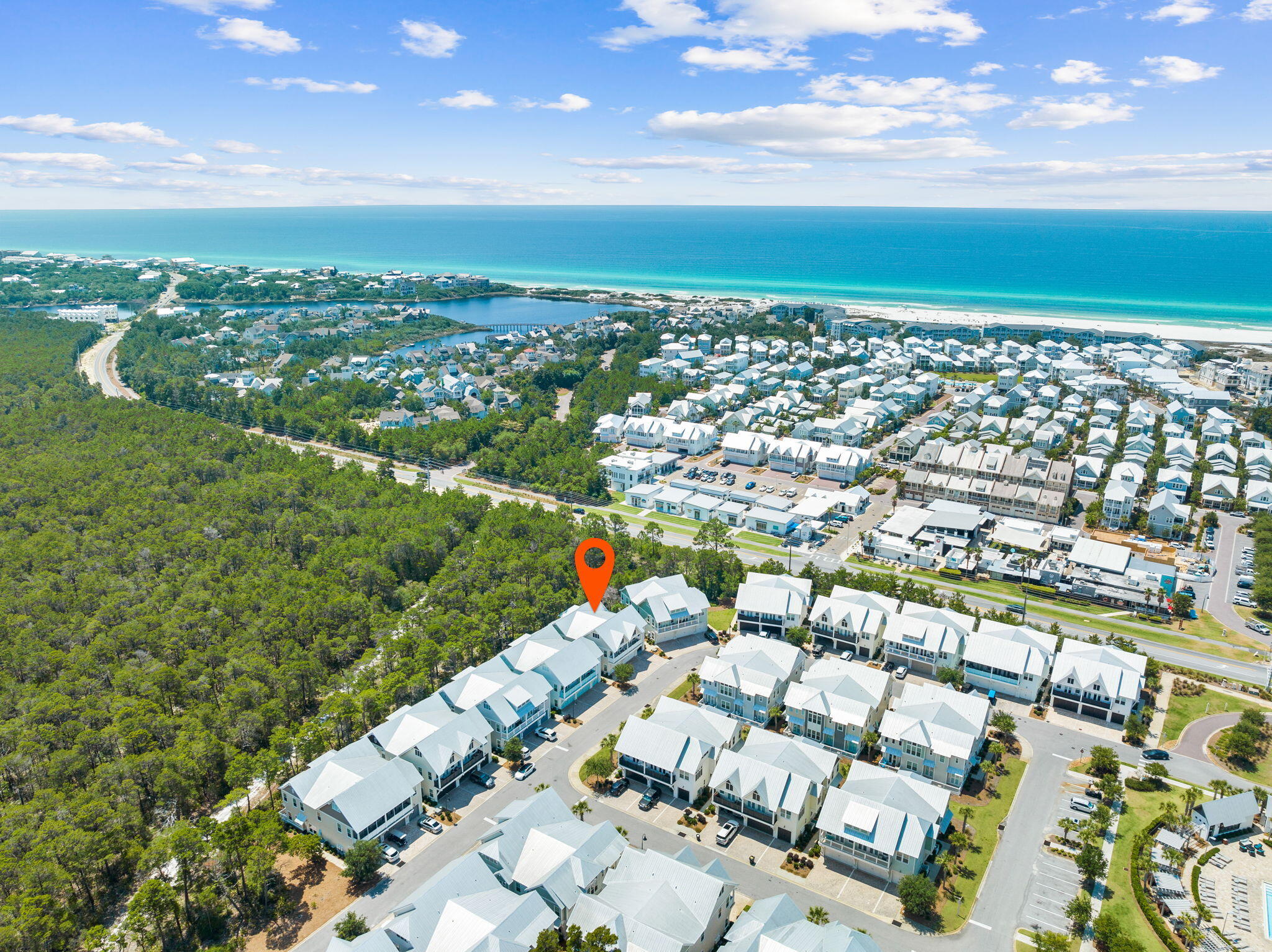 Aerial view of a coastal neighborhood, with a red pin marking a home near the beach and turquoise water.