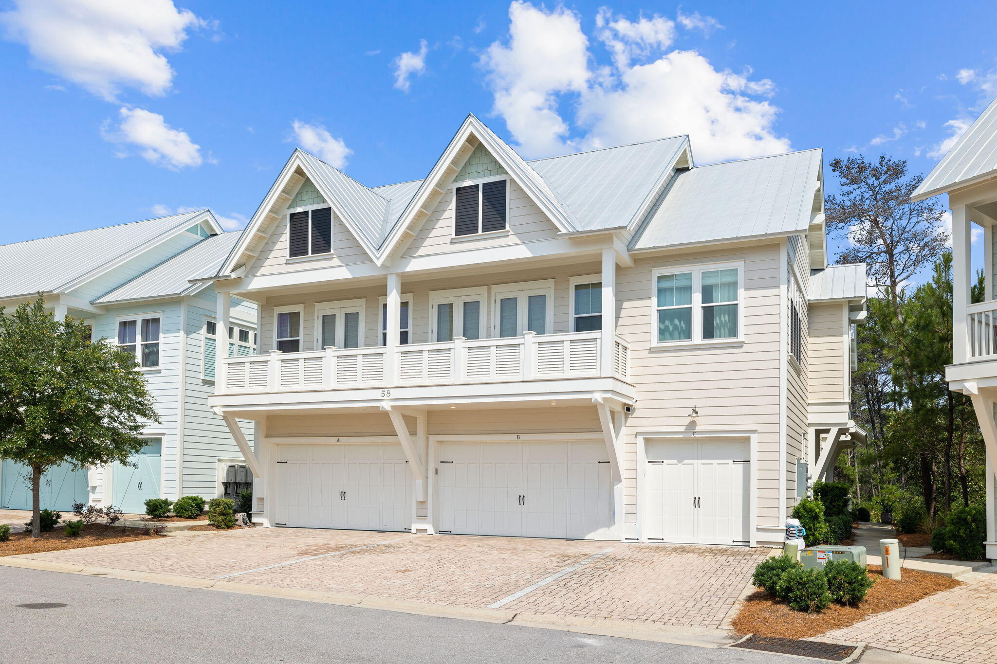 Light-colored multi-unit home with white gabled metal roofs, upper balconies, and ground-level garages.