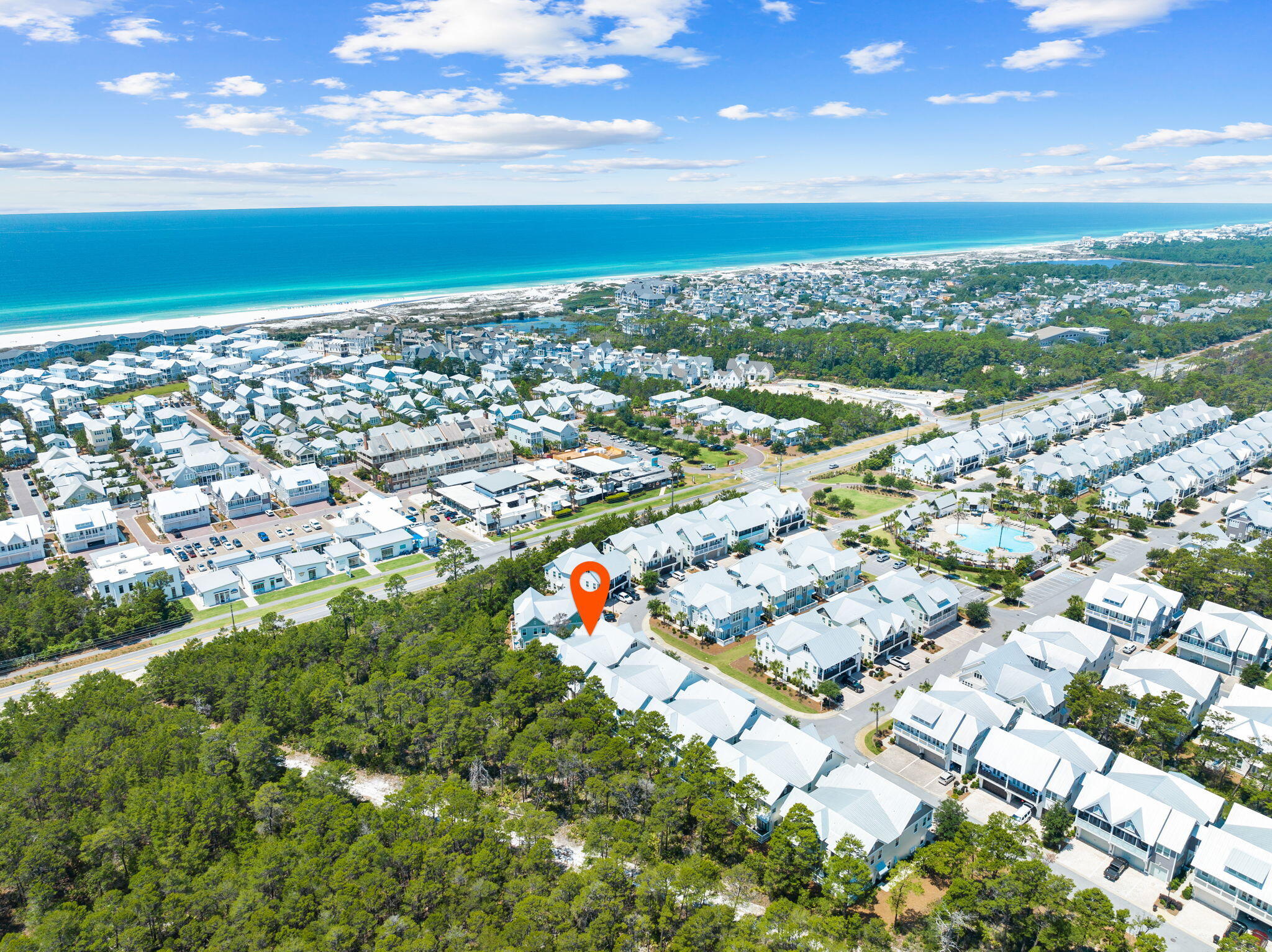 Aerial view of a coastal neighborhood, with a red marker on one home and the Gulf shoreline beyond.