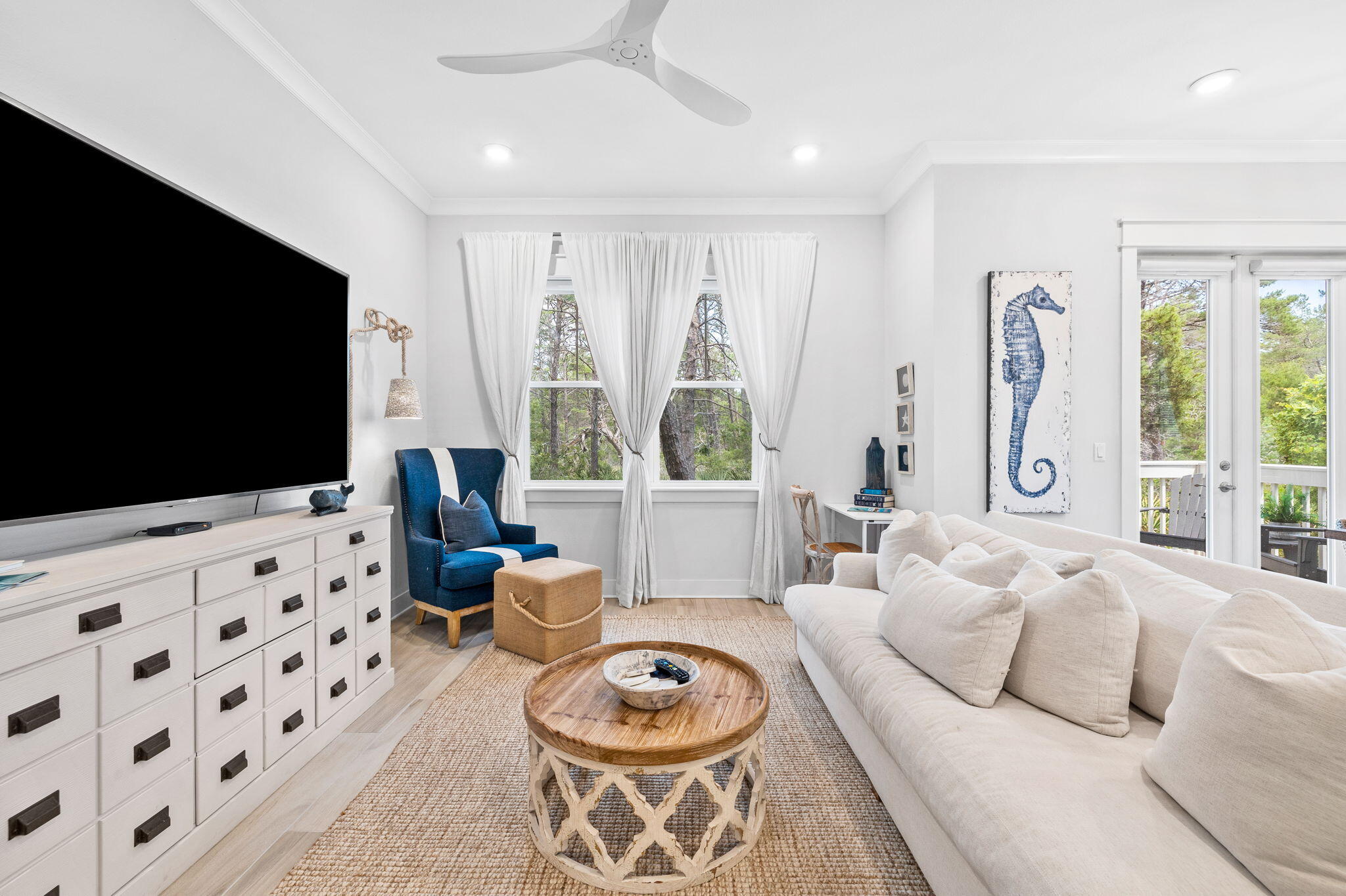 Living room with a white sofa, blue armchair, round wood coffee table, and windows overlooking trees.