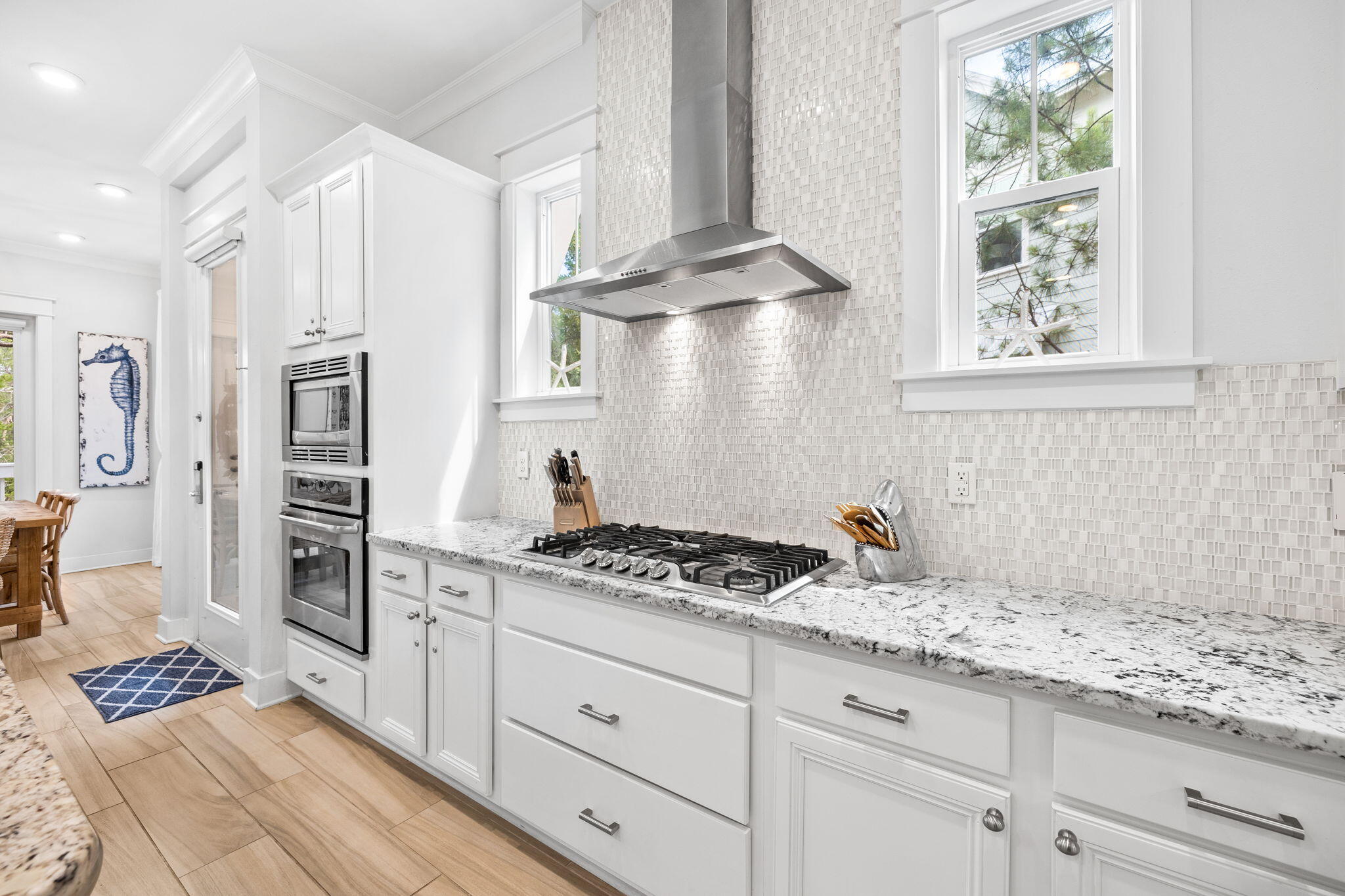 Bright white kitchen with a granite counter, mosaic backsplash, gas cooktop, and built-in ovens.