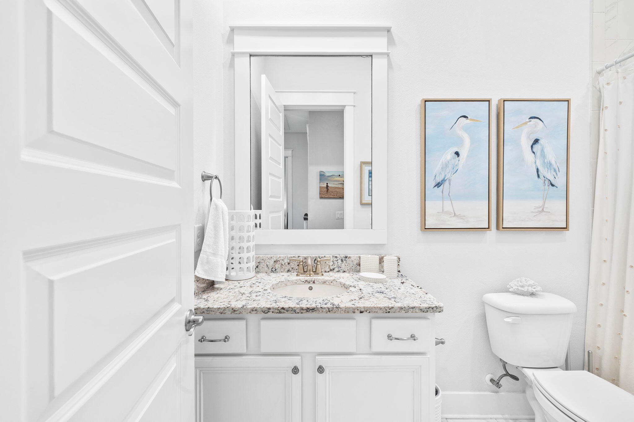 Bathroom with a granite vanity, large mirror, and framed heron artwork beside the toilet.