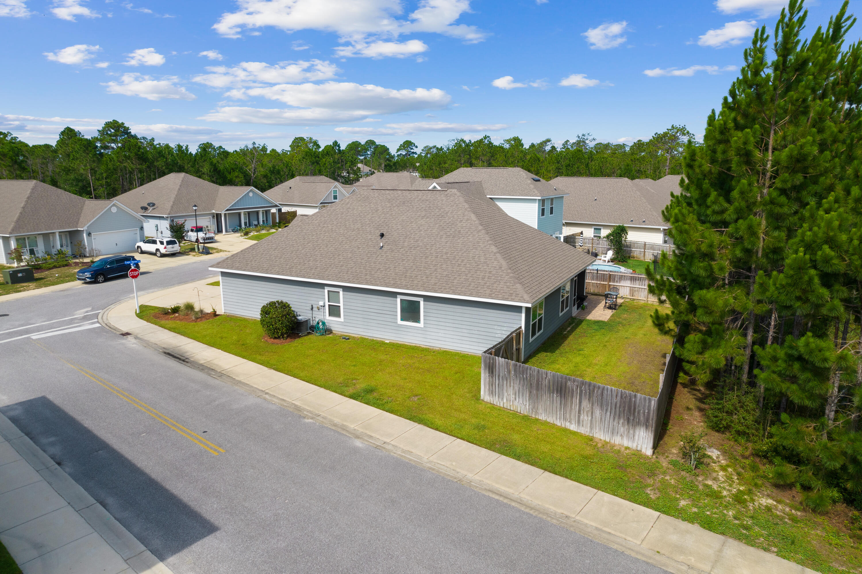 Aerial view of a gray-blue home with a fenced backyard on a tree-lined residential street.