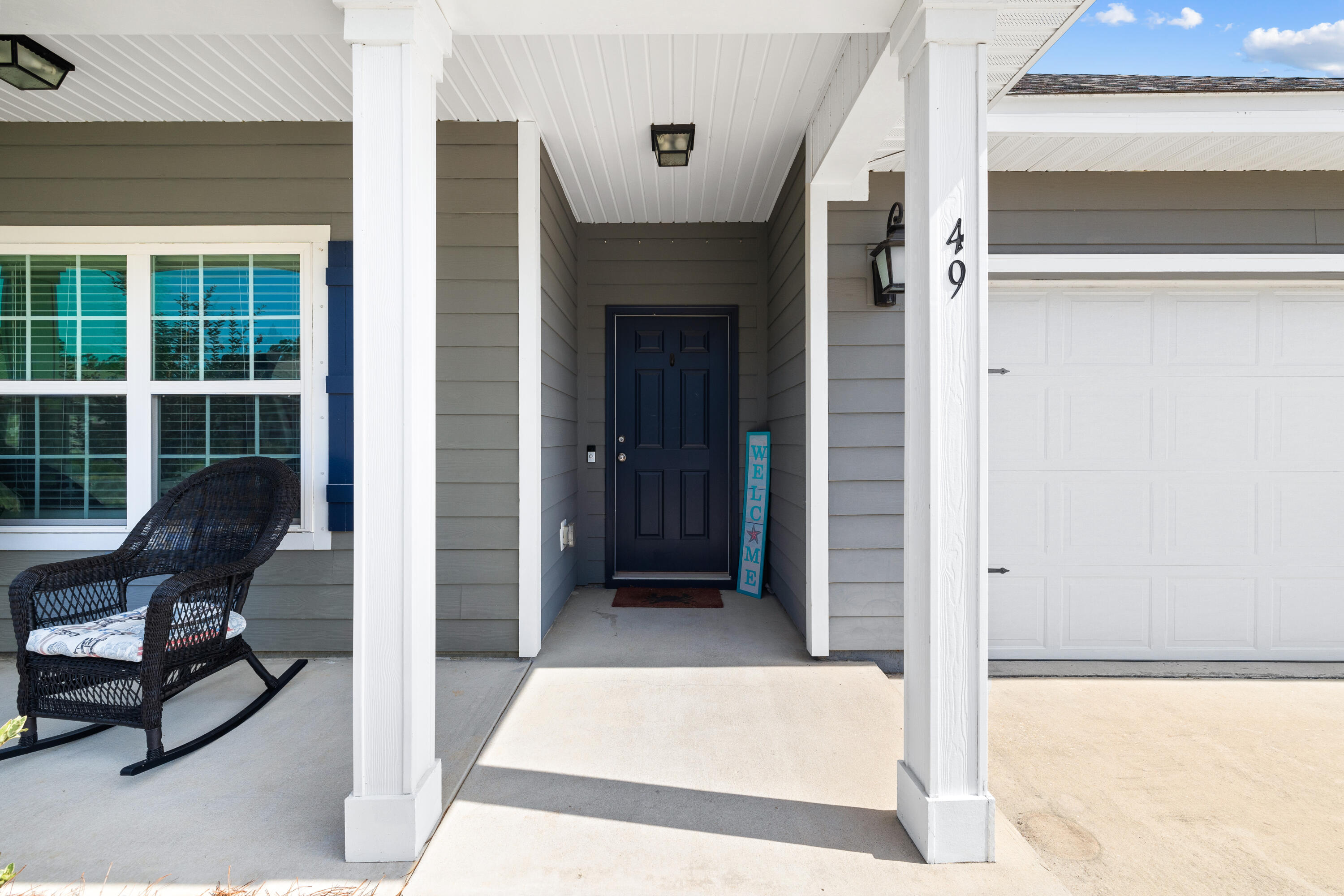 House entrance with navy door, white porch columns, wicker rocking chair, and attached garage.