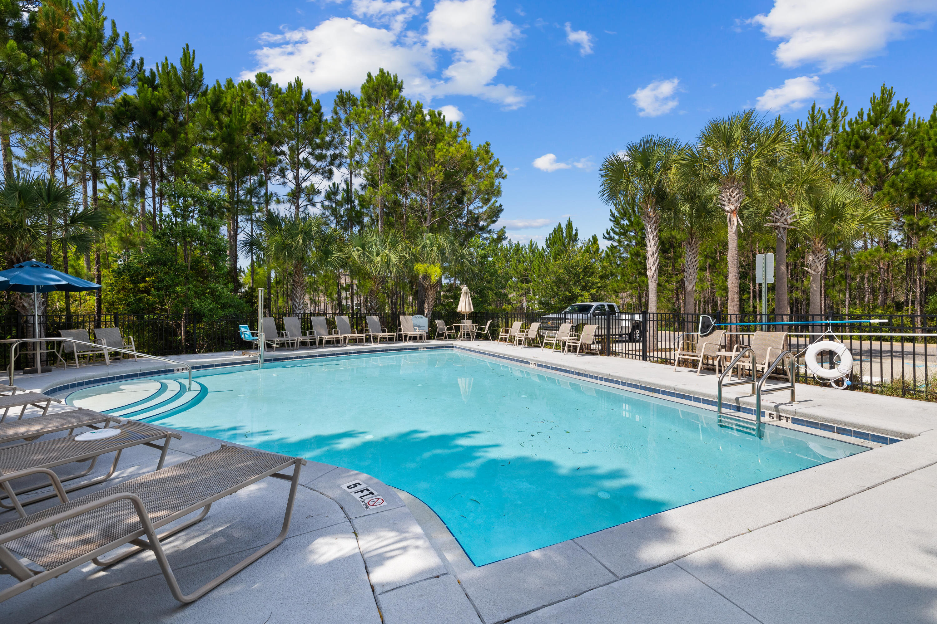 Outdoor swimming pool with turquoise water, lounge chairs, and pine and palm trees.