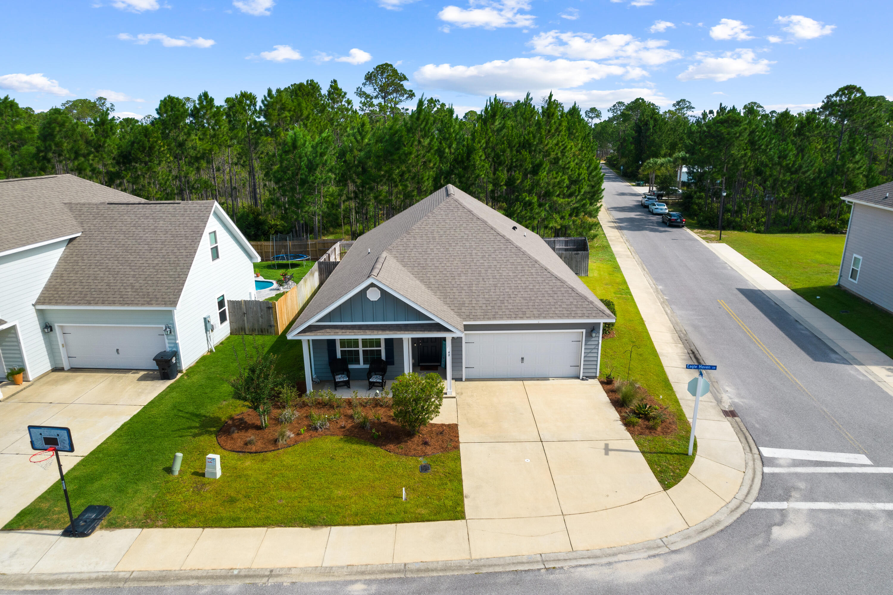 Gray-blue corner house with a covered porch, attached garage, and wooded backdrop.
