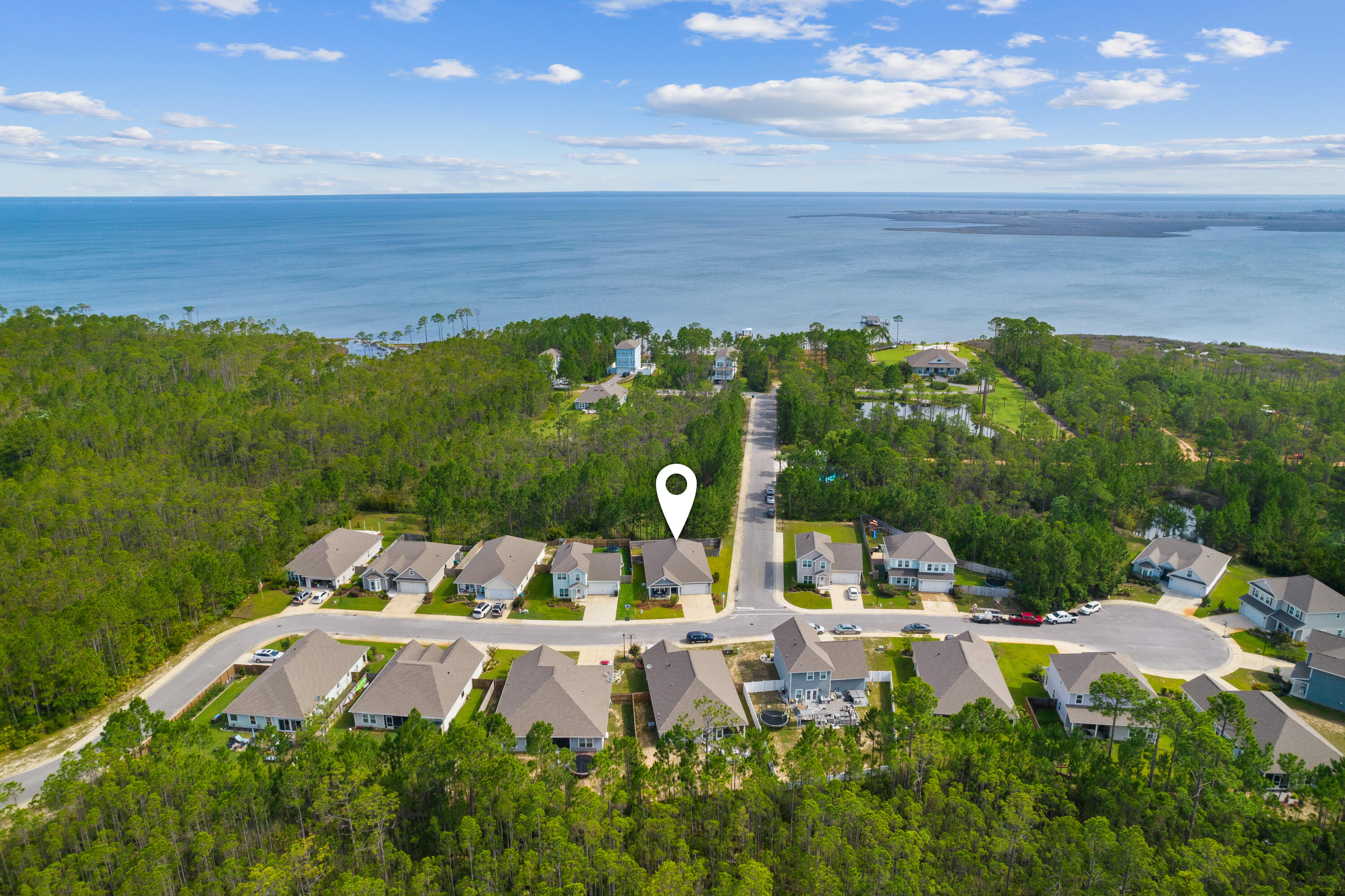 Aerial view of the marked home in a wooded neighborhood beside coastal water.