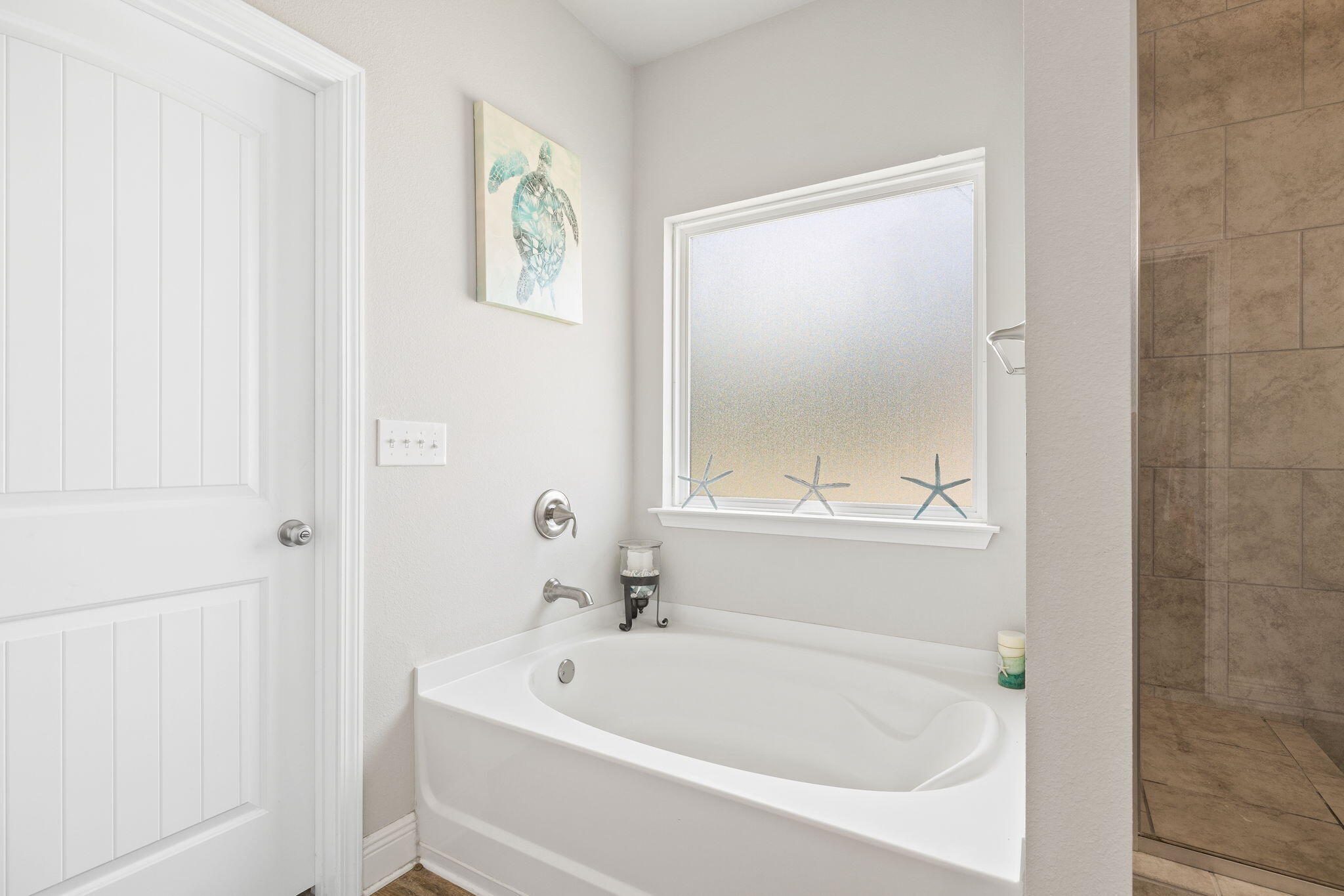 Bathroom with a white soaking tub, starfish on the window sill, and a tiled shower.