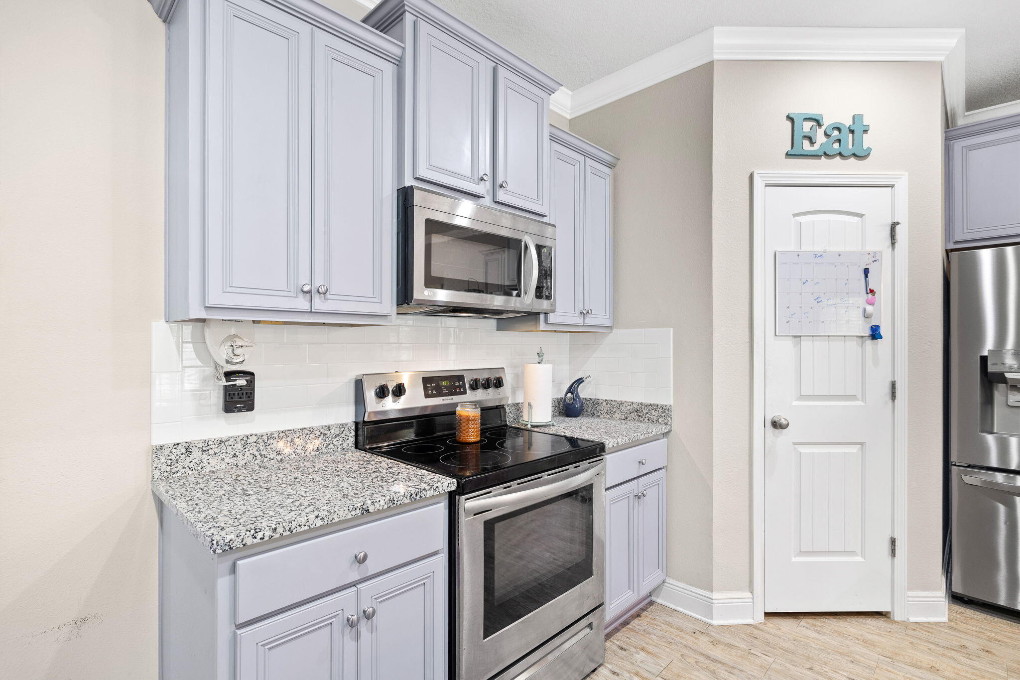 Kitchen with gray cabinets, granite counters, stainless appliances, and an “Eat” sign above the pantry door.