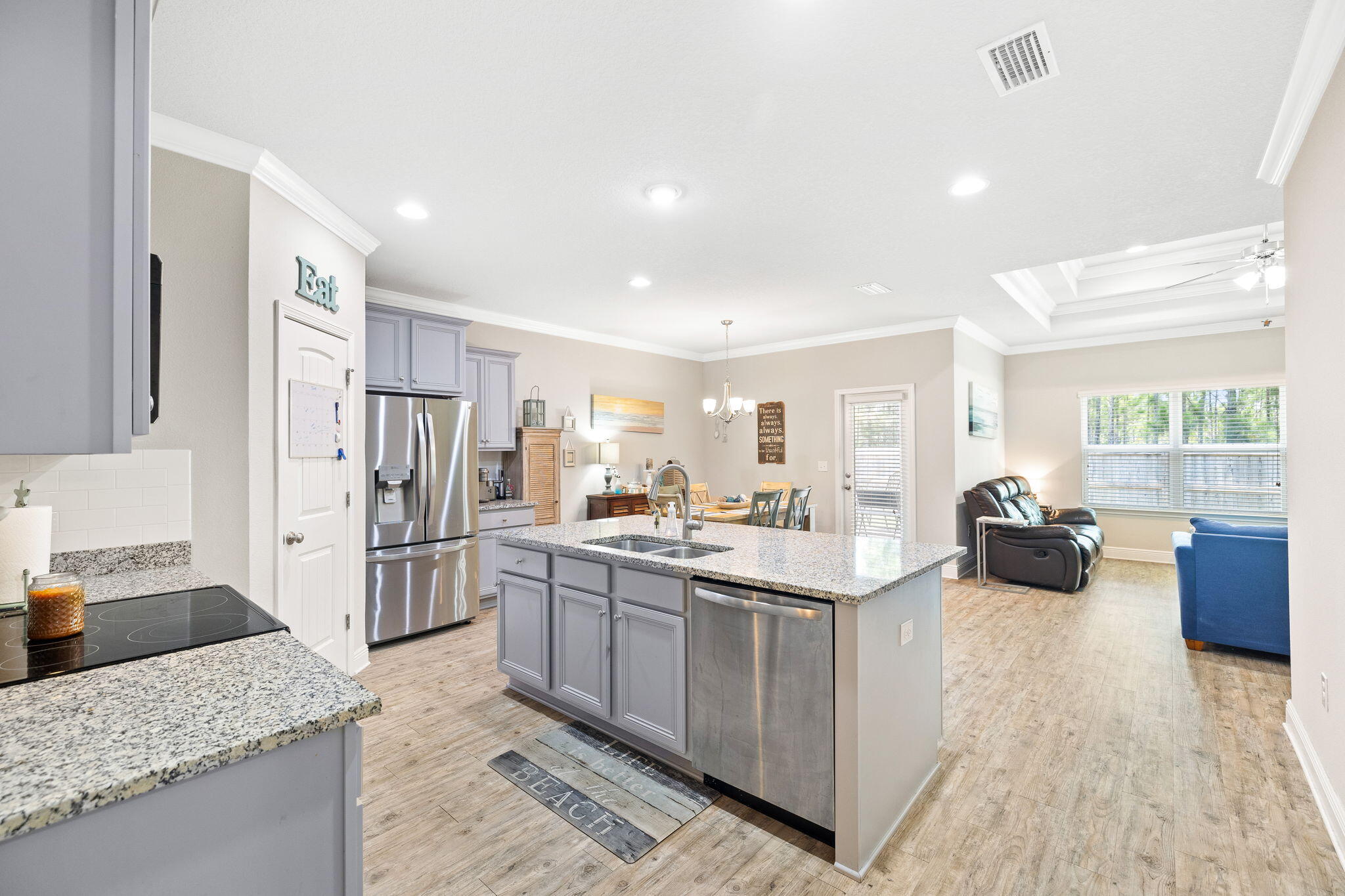Open-plan kitchen with a granite island, gray cabinets, stainless appliances, and living room beyond.