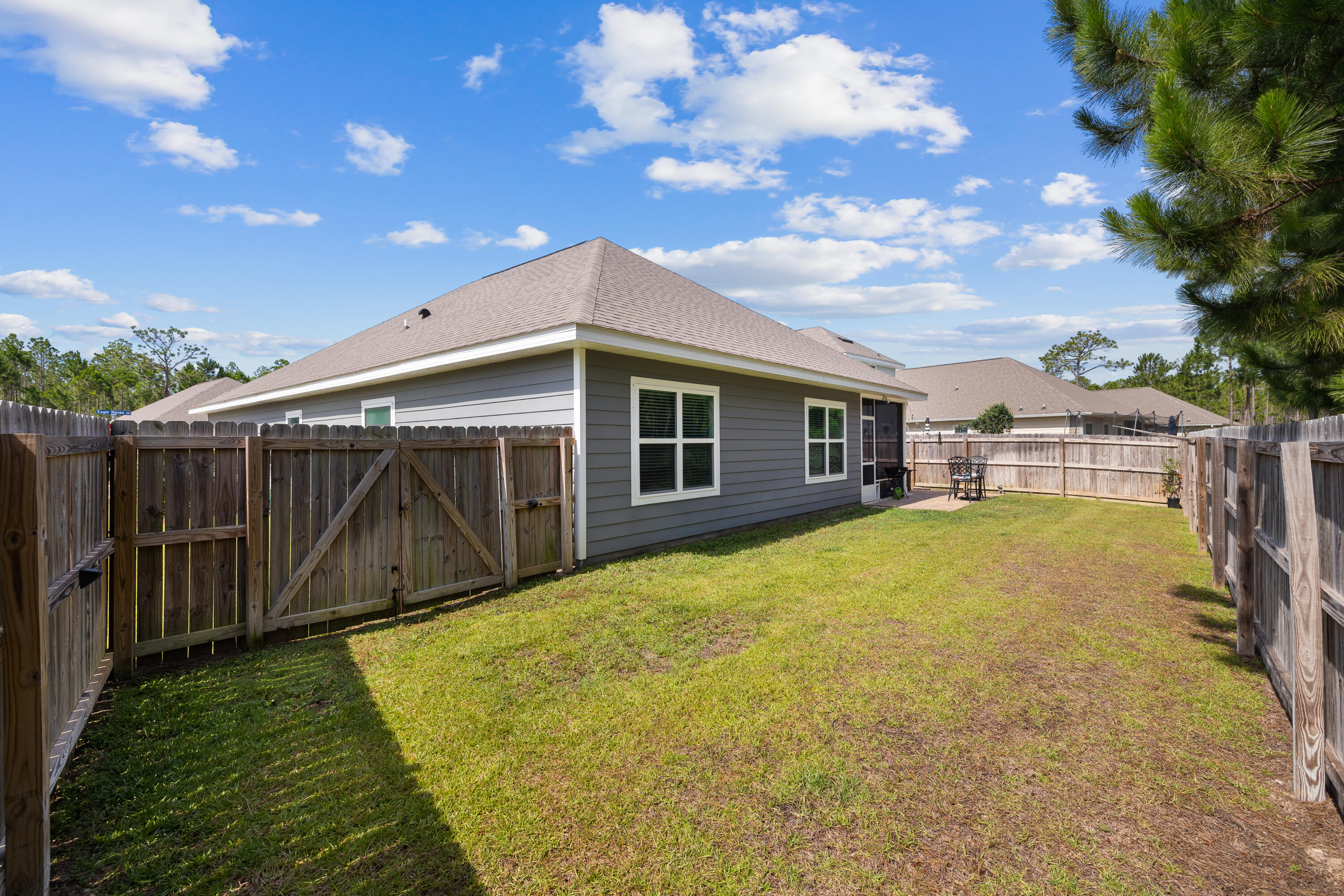 Gray house behind a wooden fence, with a grassy backyard, gate, and small patio table.