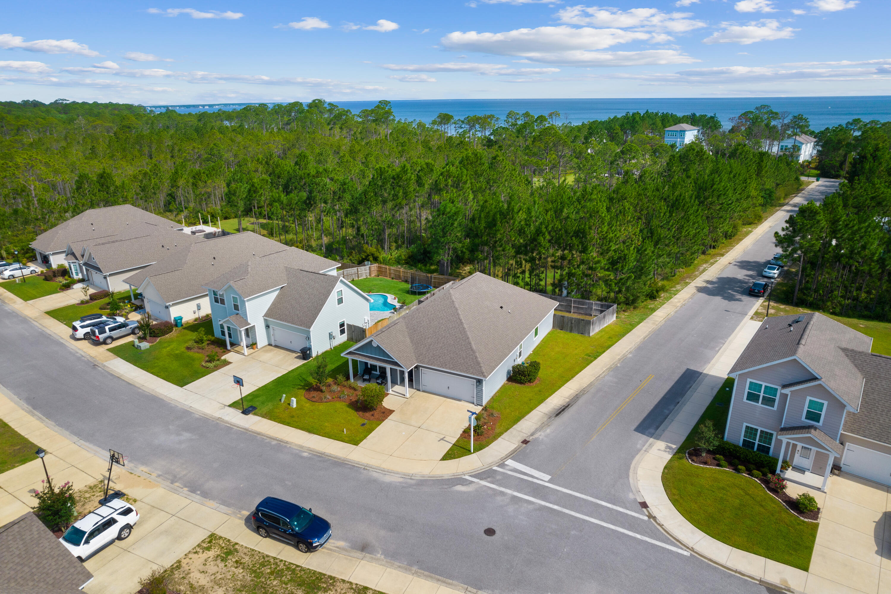 Aerial view of a coastal home beside wooded land, with blue water visible beyond.