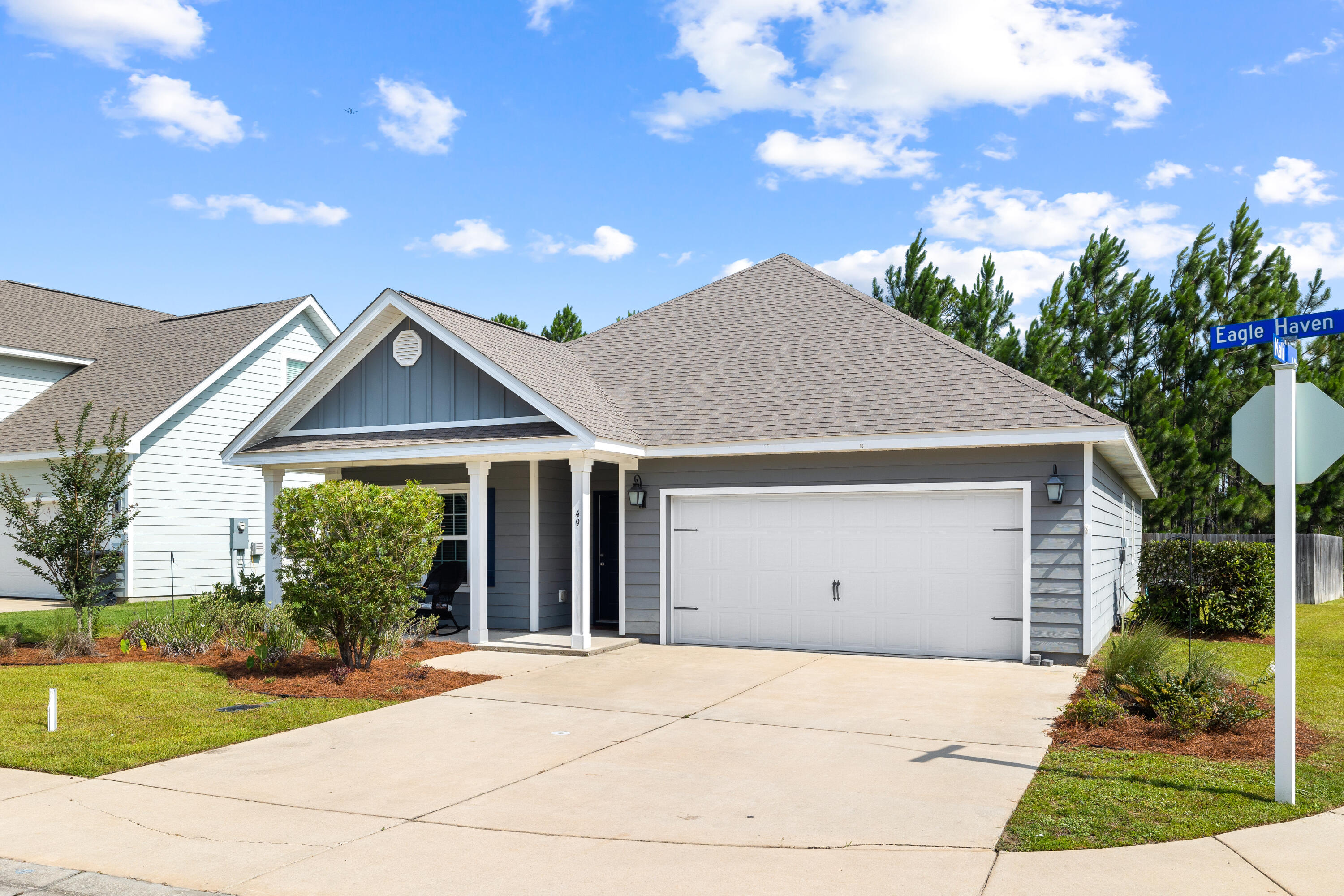 Gray single-story home with a white double garage, covered porch, and wide driveway beside an Eagle Haven street sign.