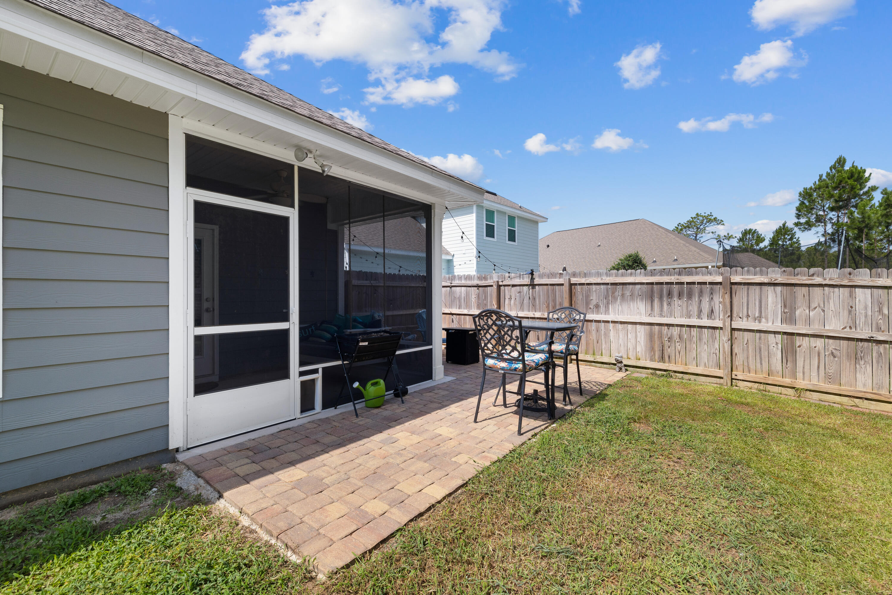 Backyard brick patio beside a screened porch, with outdoor dining furniture and a fenced lawn.