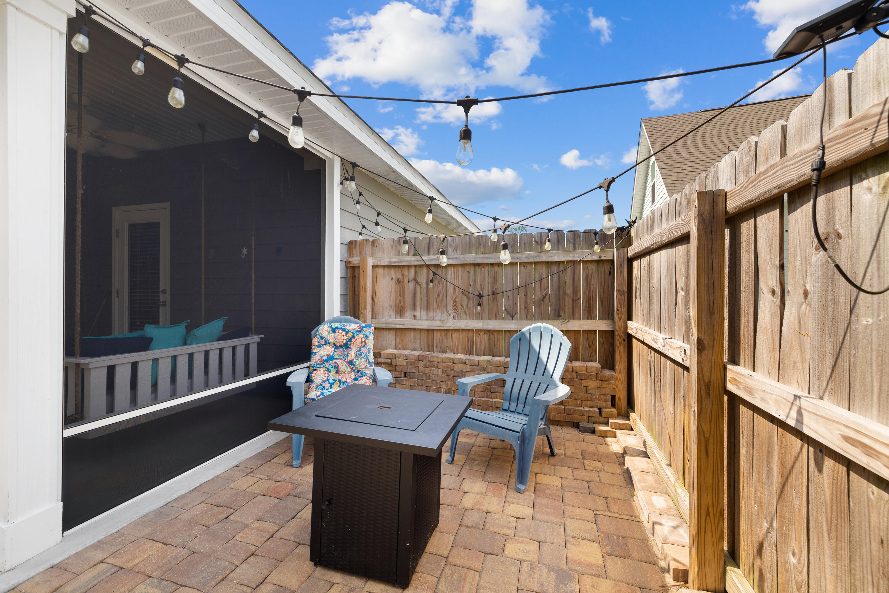 Fenced brick patio with outdoor chairs, a table, overhead string lights, and an adjoining screened porch.