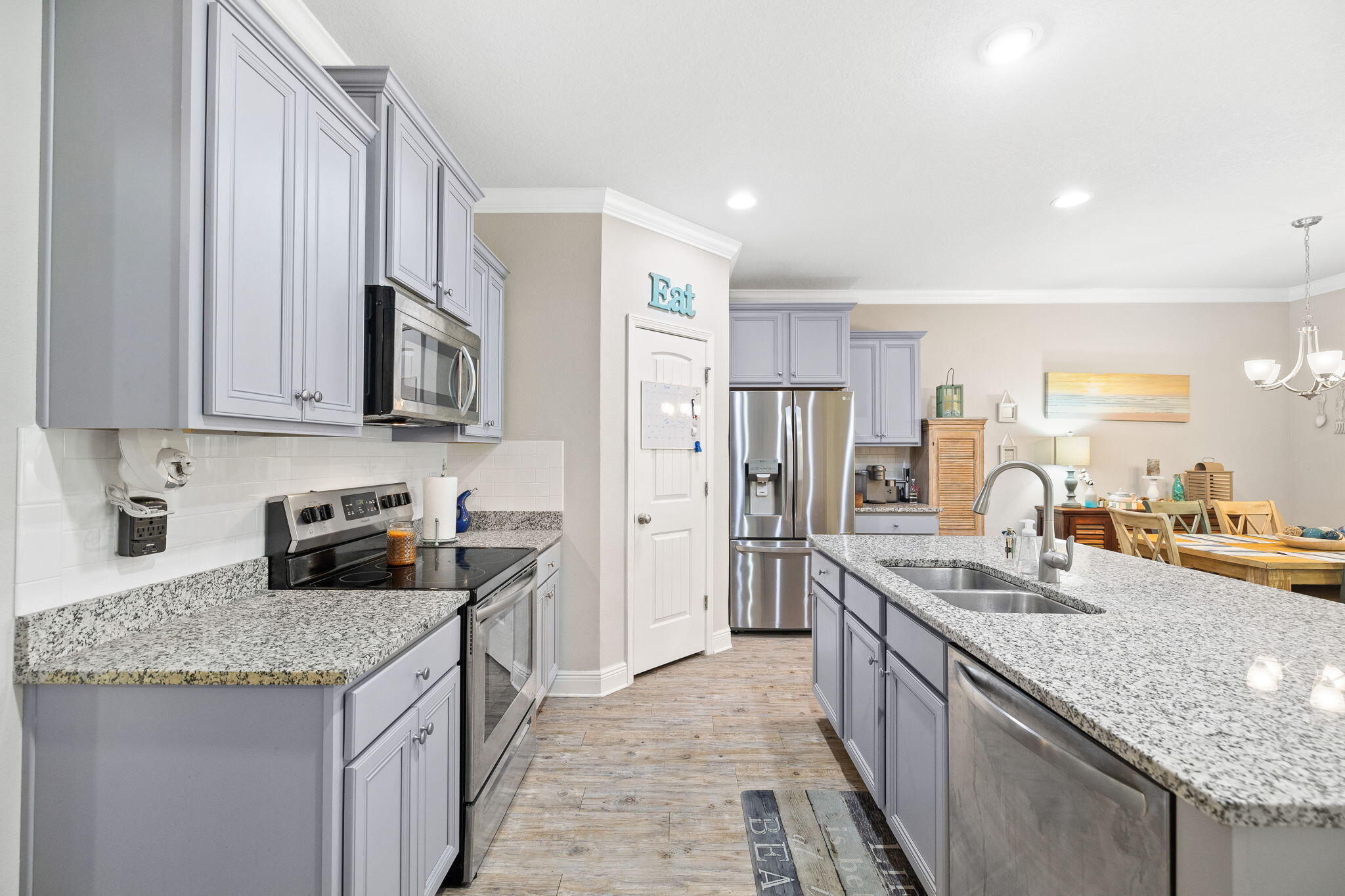 Kitchen with pale gray cabinets, granite counters, stainless steel appliances, and an island sink beside a dining area.