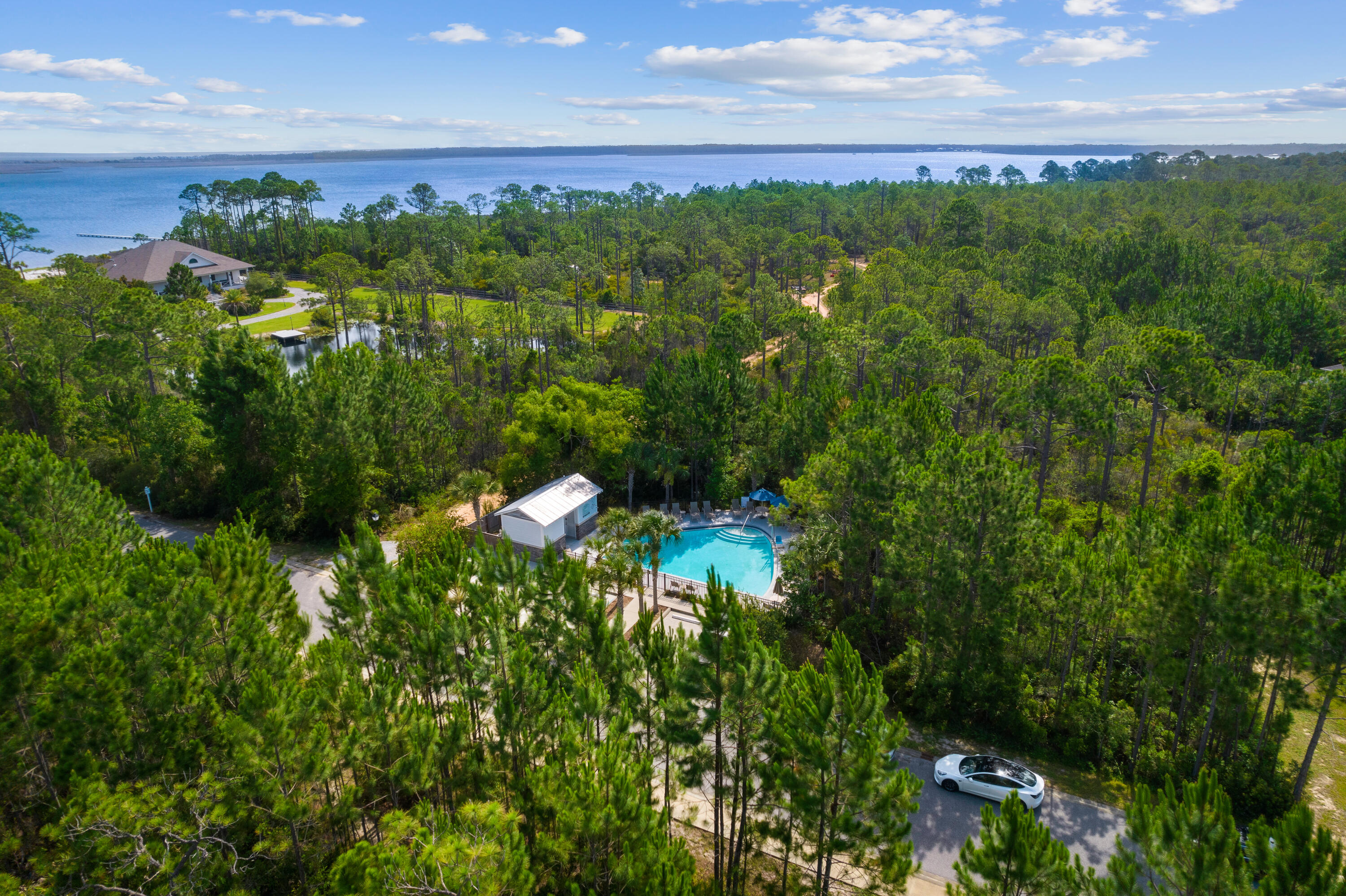 Aerial view of a wooded property with a swimming pool and broad bay beyond.