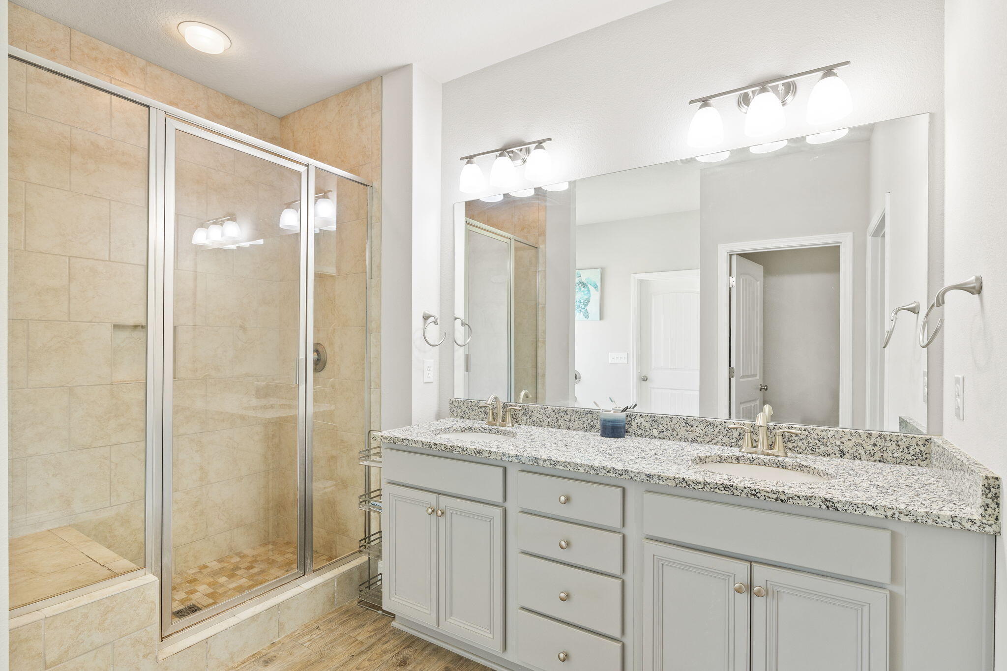 Bathroom with double-sink vanity and granite countertop beside a glass-enclosed tile shower.