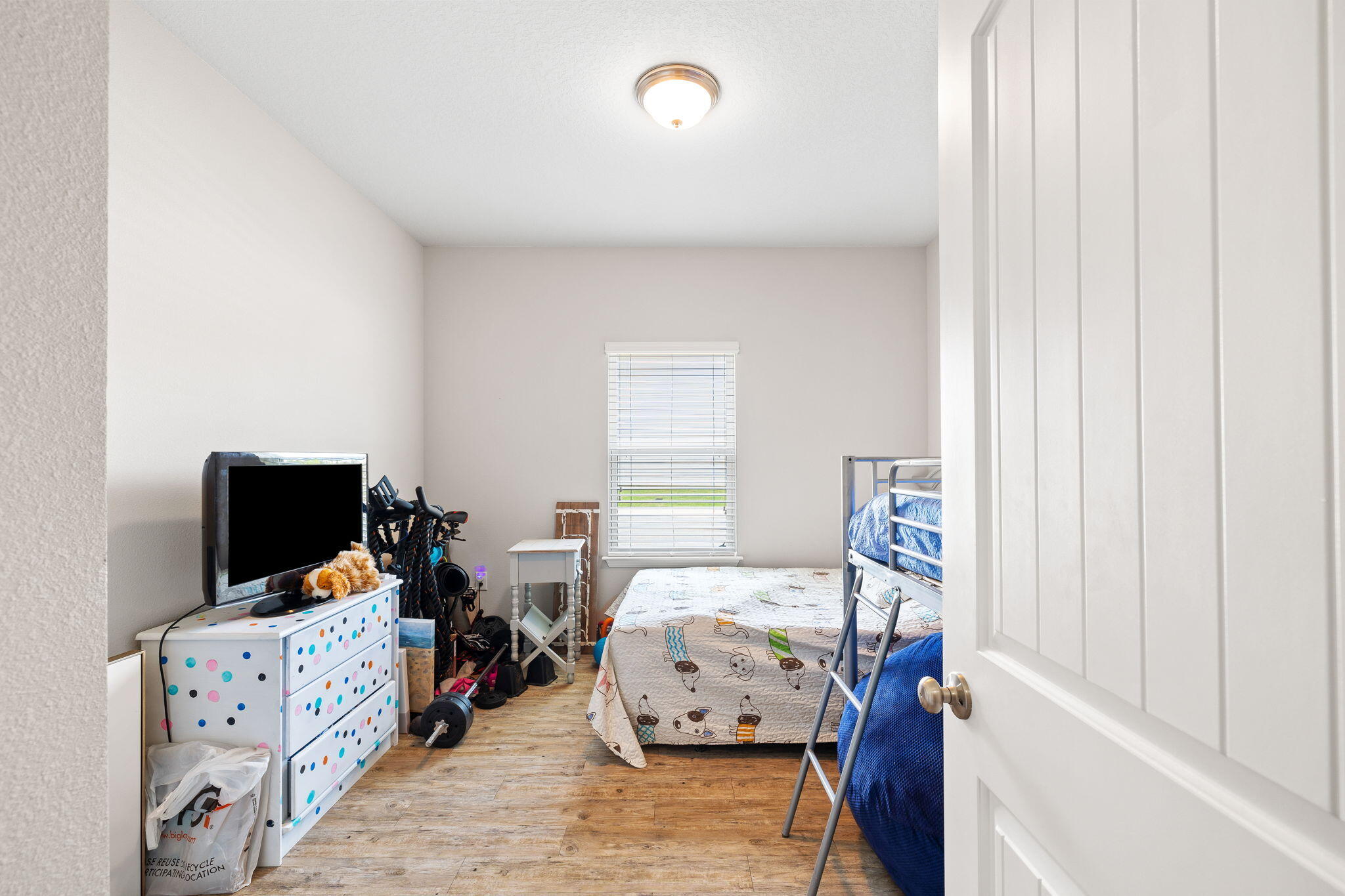 Bedroom with a single bed, metal bunk bed, polka-dot dresser, and exercise equipment.