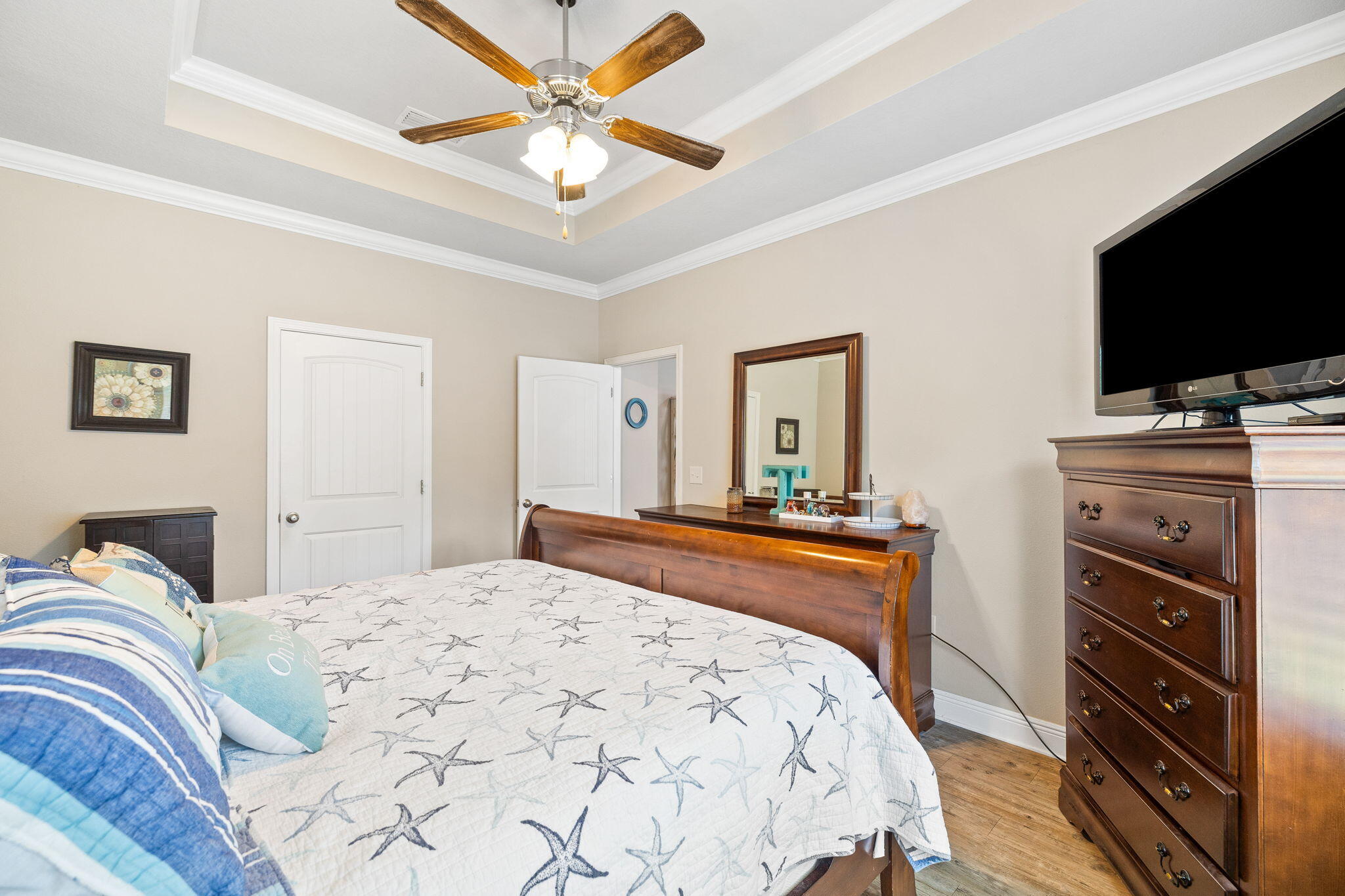 Bedroom with starfish-patterned bedding, a tray ceiling, and wooden furniture.