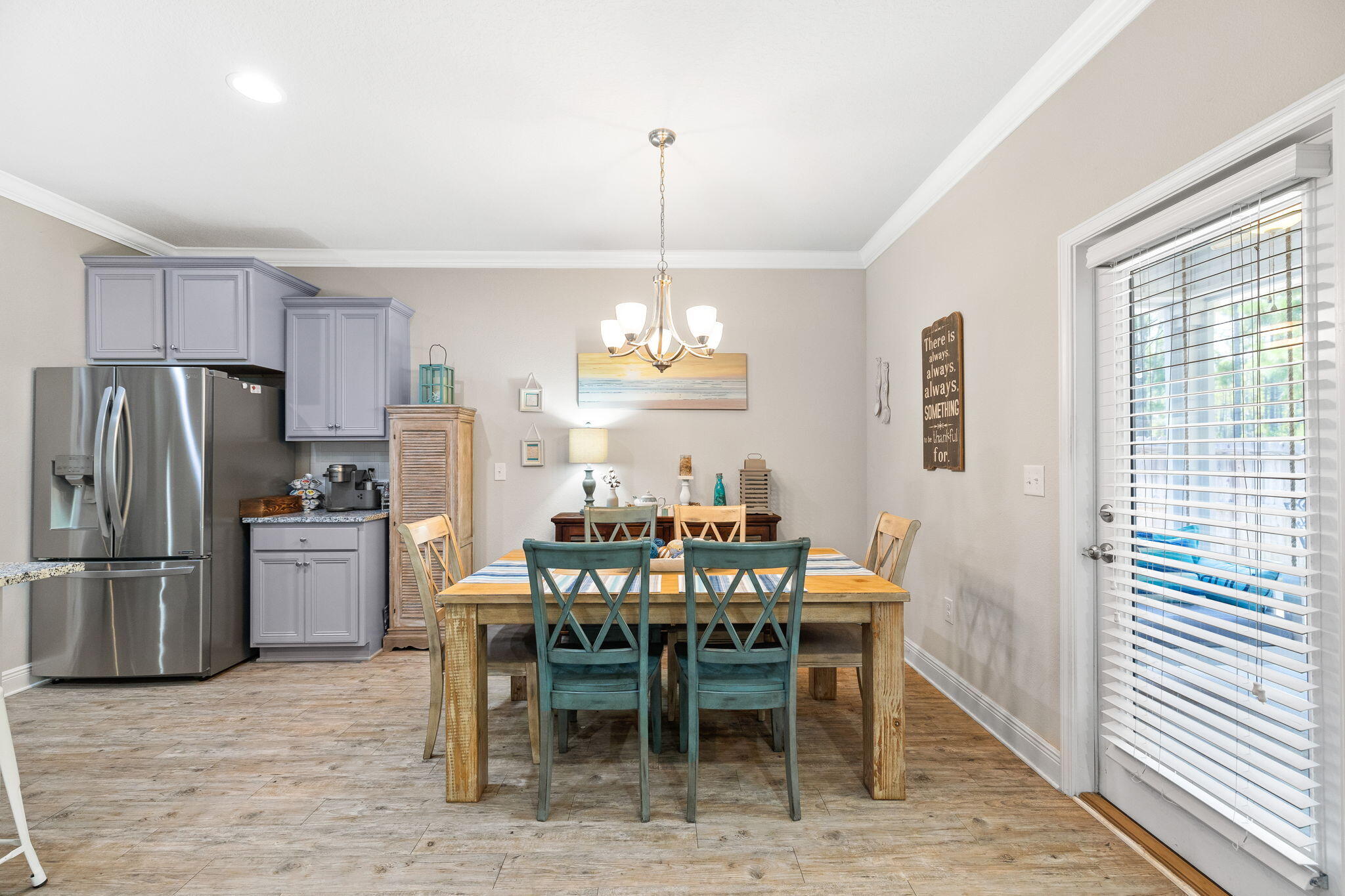 Dining area with a rustic wood table, teal chairs, gray kitchen cabinets, and a stainless-steel refrigerator.